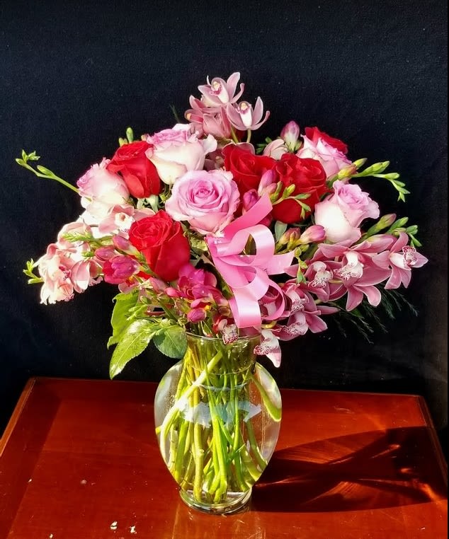 Pink and red roses with orchids in a glass vase