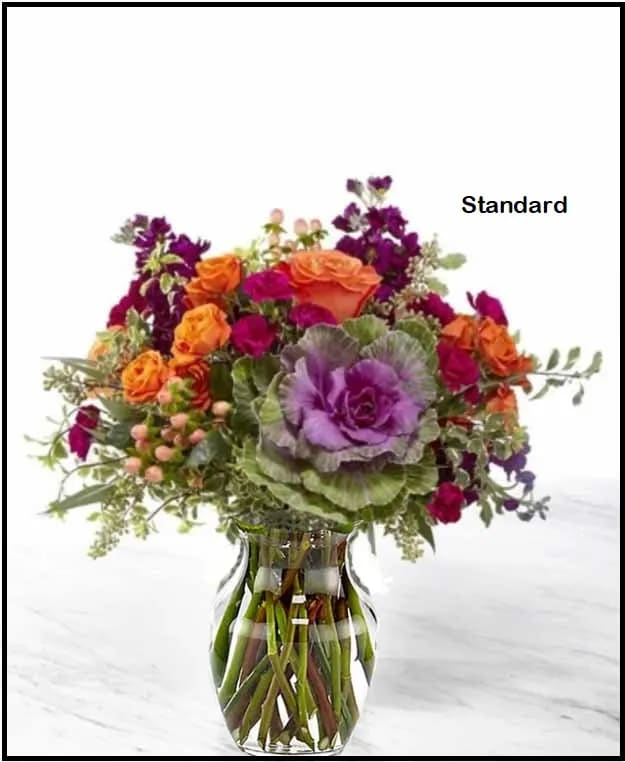 Pretty Sunset Bouquet - Premium - The  Bouquet is both simple and simply unforgettable. This collection of flowers takes all the vibrant colors fall and brings them together in a unique way in a muted green ceramic vase with a gold metallic finish. Ornamental kale is surrounded by orange roses, spray roses and purple stock making the perfect gift for you or your loved ones. GOOD bouquet is approx. 14"H x 15"W. BETTER bouquet is approx. 16"H x 17"W. BEST bouquet is approx. 16"H x 19"W.  