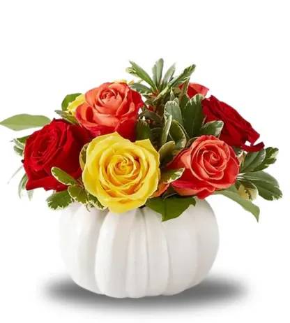 Red, yellow, and coral roses in a white pumpkin vase