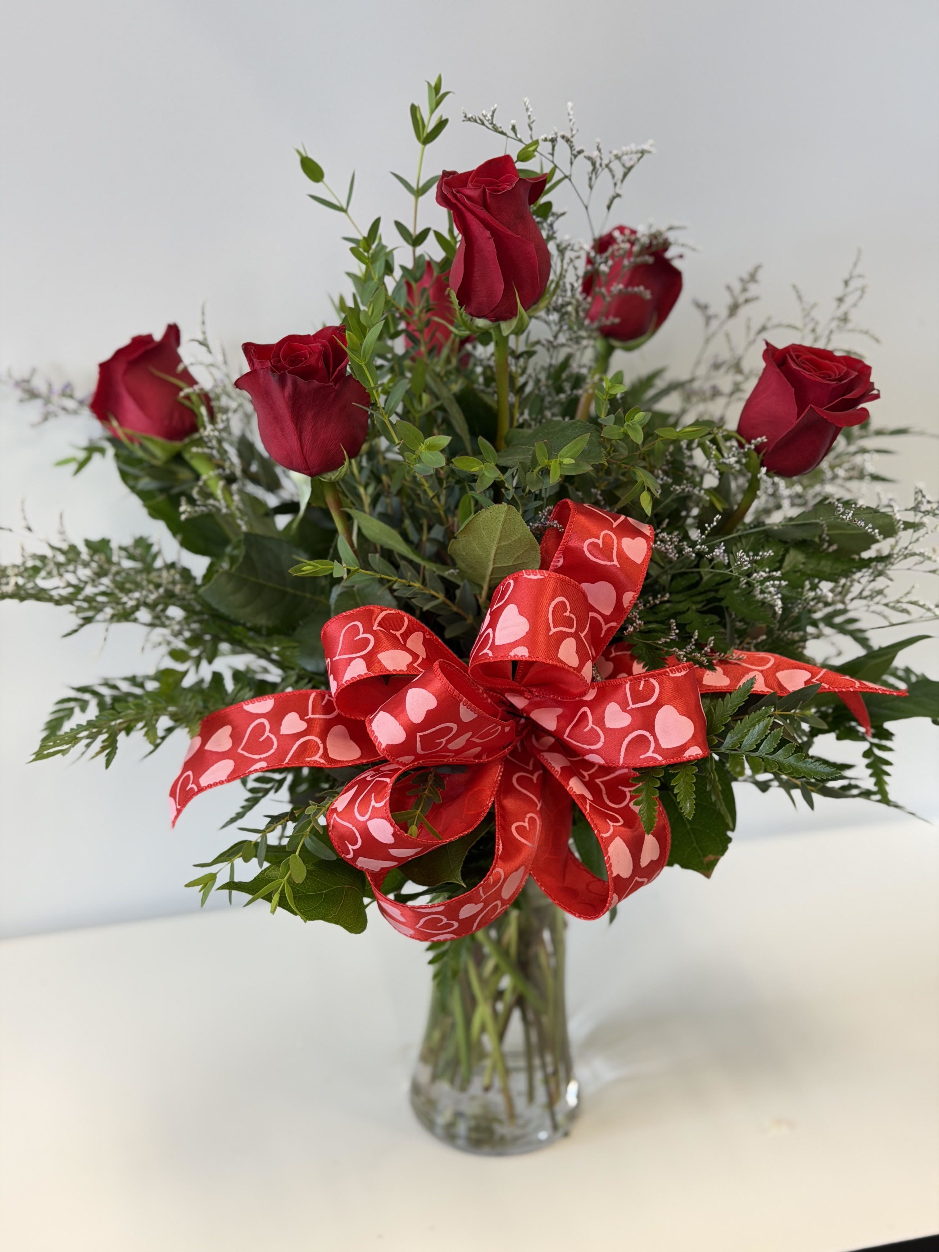 Red roses in a clear glass vase with a heart-patterned ribbon