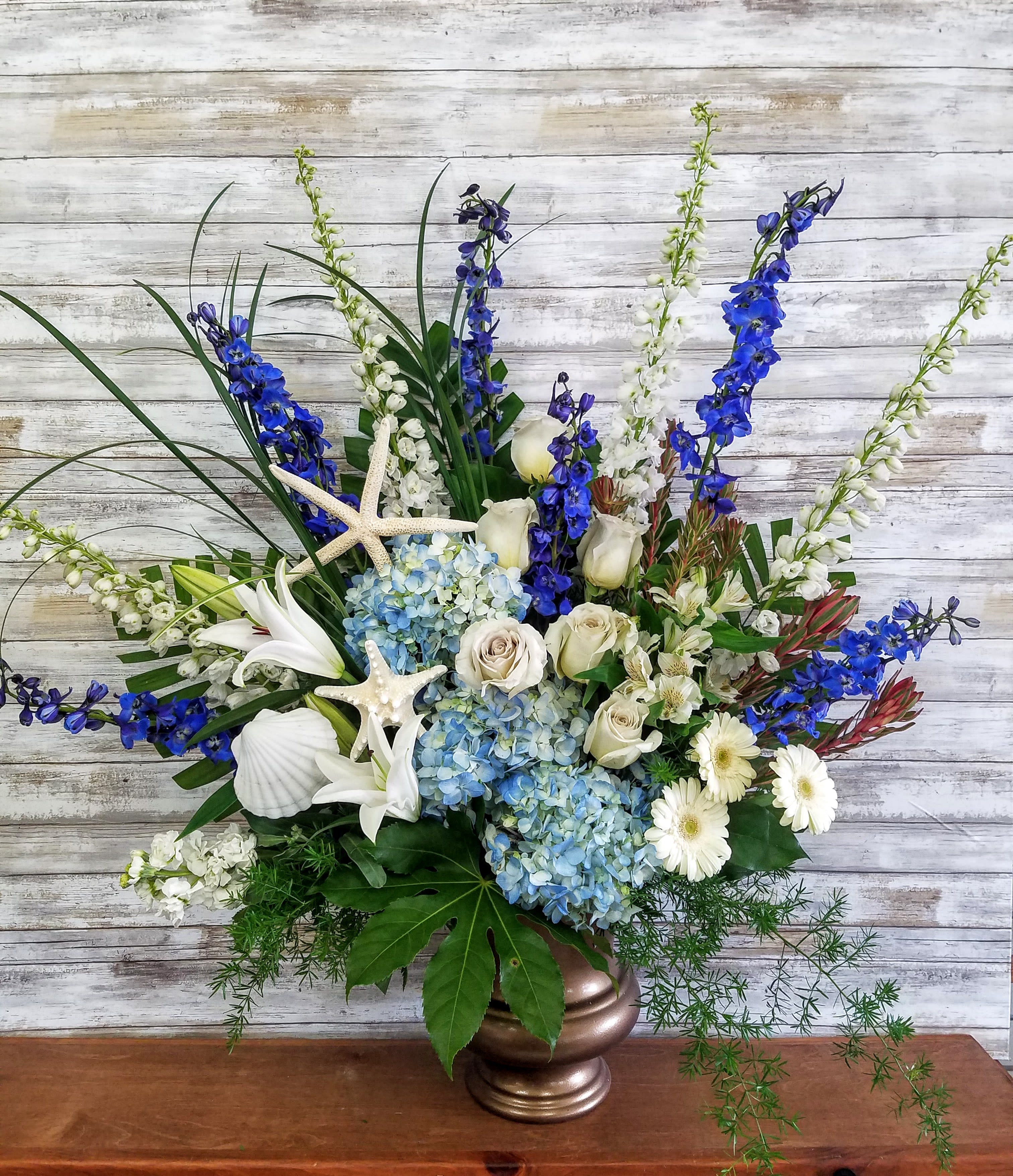 Blue and white floral arrangement in a bronze vase with starfish accents