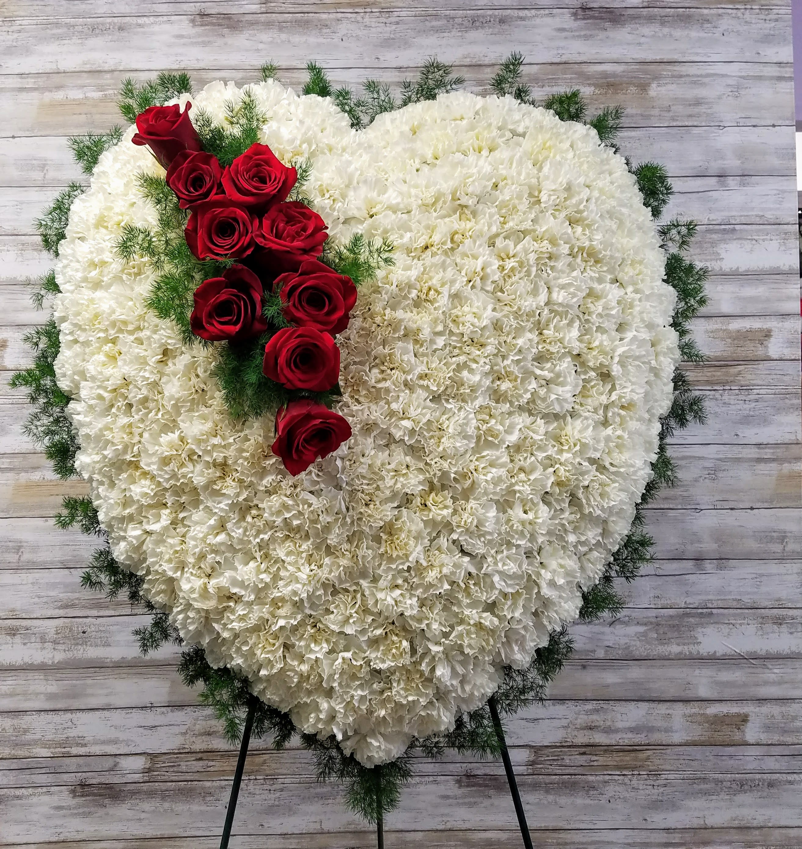 Heart-shaped white floral spray with red roses on a stand