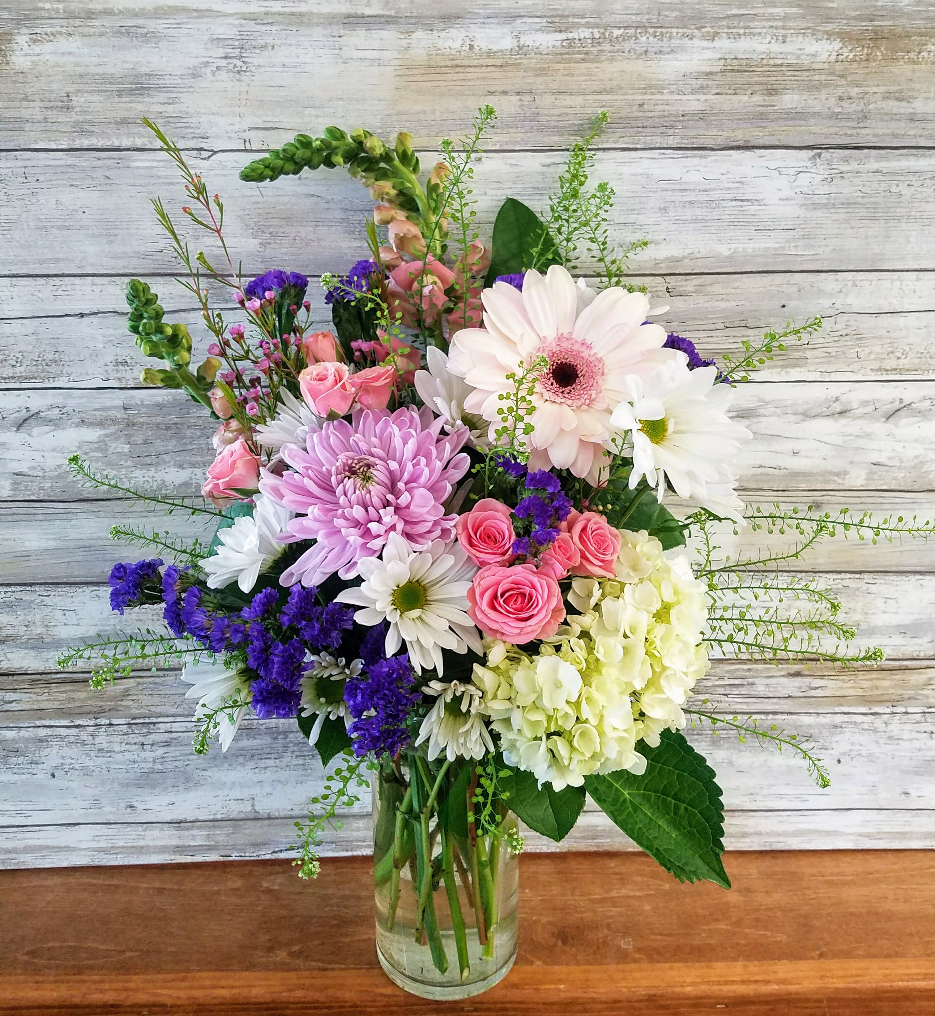 Mixed bouquet of pink, white, and purple flowers in a clear glass vase