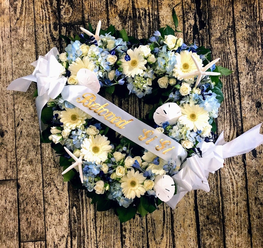 Heart-shaped floral wreath with white ribbon and pale blue flowers