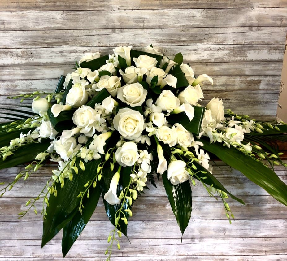 White roses and calla lilies arranged with orchids and broad leaves