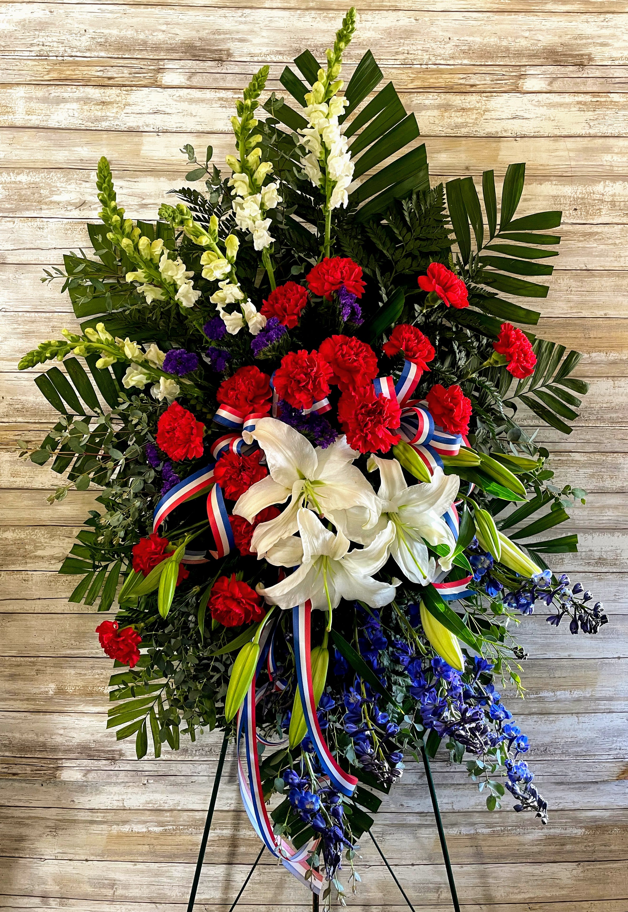 Sacred Duty Spray - Standing tall, proud and patriotic, this dazzling free-standing spray is like a fireworks display made of graceful flowers. Uniquely beautiful, it's a lovely way to honor a great loss. 