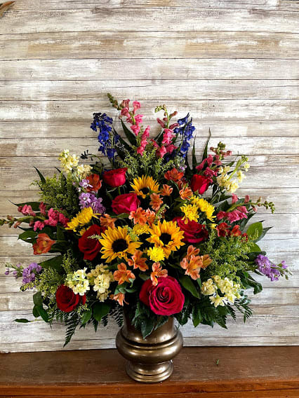 Large mixed flower arrangement in a gold vase with red, yellow, pink, and purple blooms