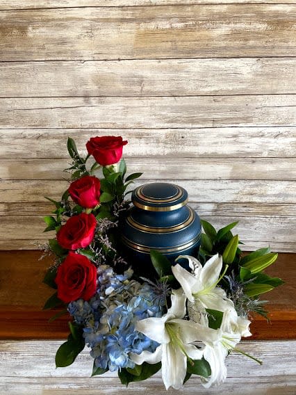 Red roses and white lilies arranged around a blue urn