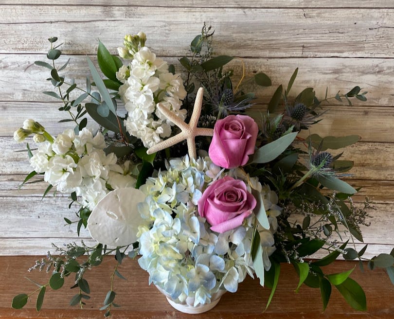 Pink roses and white flowers arranged with a starfish in a white vase