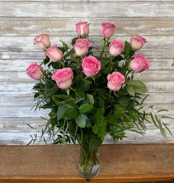 Pink roses arranged in a clear glass vase with mixed greenery