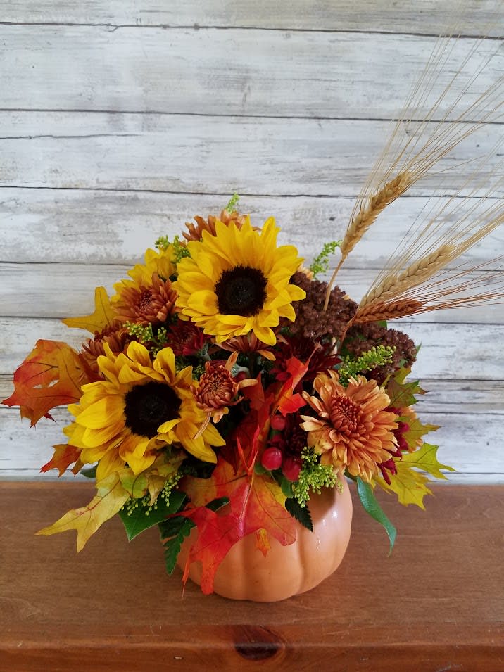 Pretty Pumpkin- One Sided Arrangement  - Our Pumpkin arrangement is always a Fall Favorite. Sunflowers, berries and assorted fall flowers are arranged in a delightful ceramic pumpkin that can be enjoyed for many seasons to come.   Approx. 12" Tall   Substitutions may be made based on seasonal availability. 