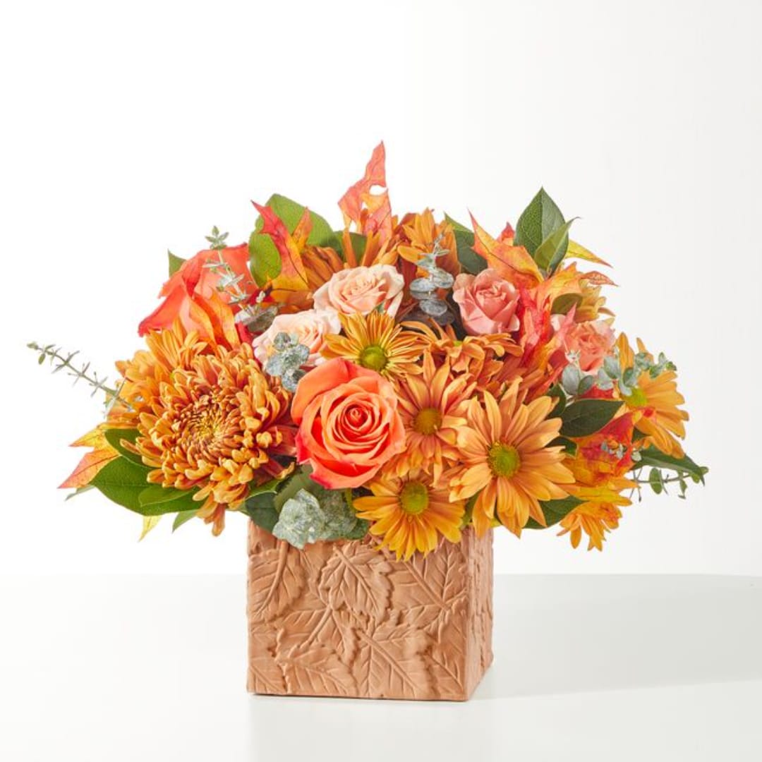 Autumn bouquet of orange and pink flowers in a textured square vase