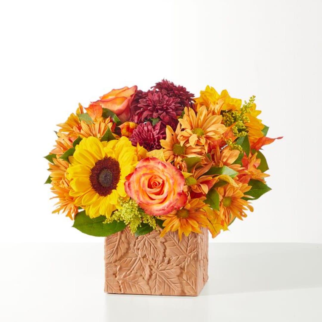 Mixed bouquet with sunflowers, roses, and orange mums in a square vase