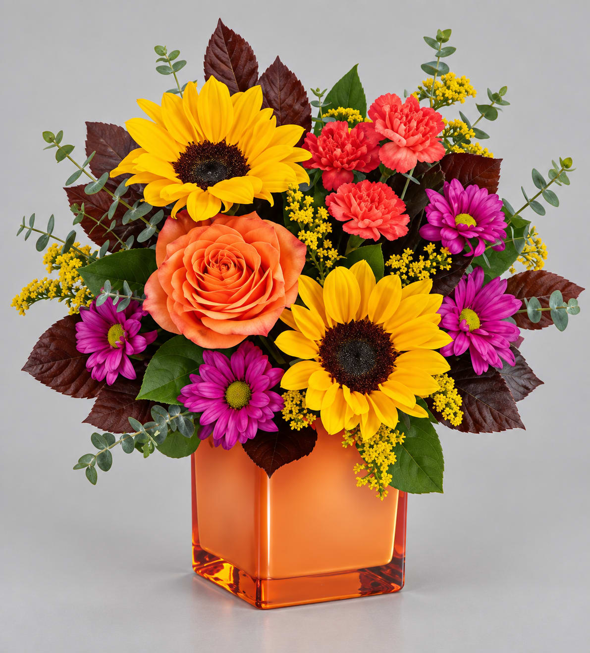 Mixed bouquet with sunflowers, roses, and daisies in an orange glass vase