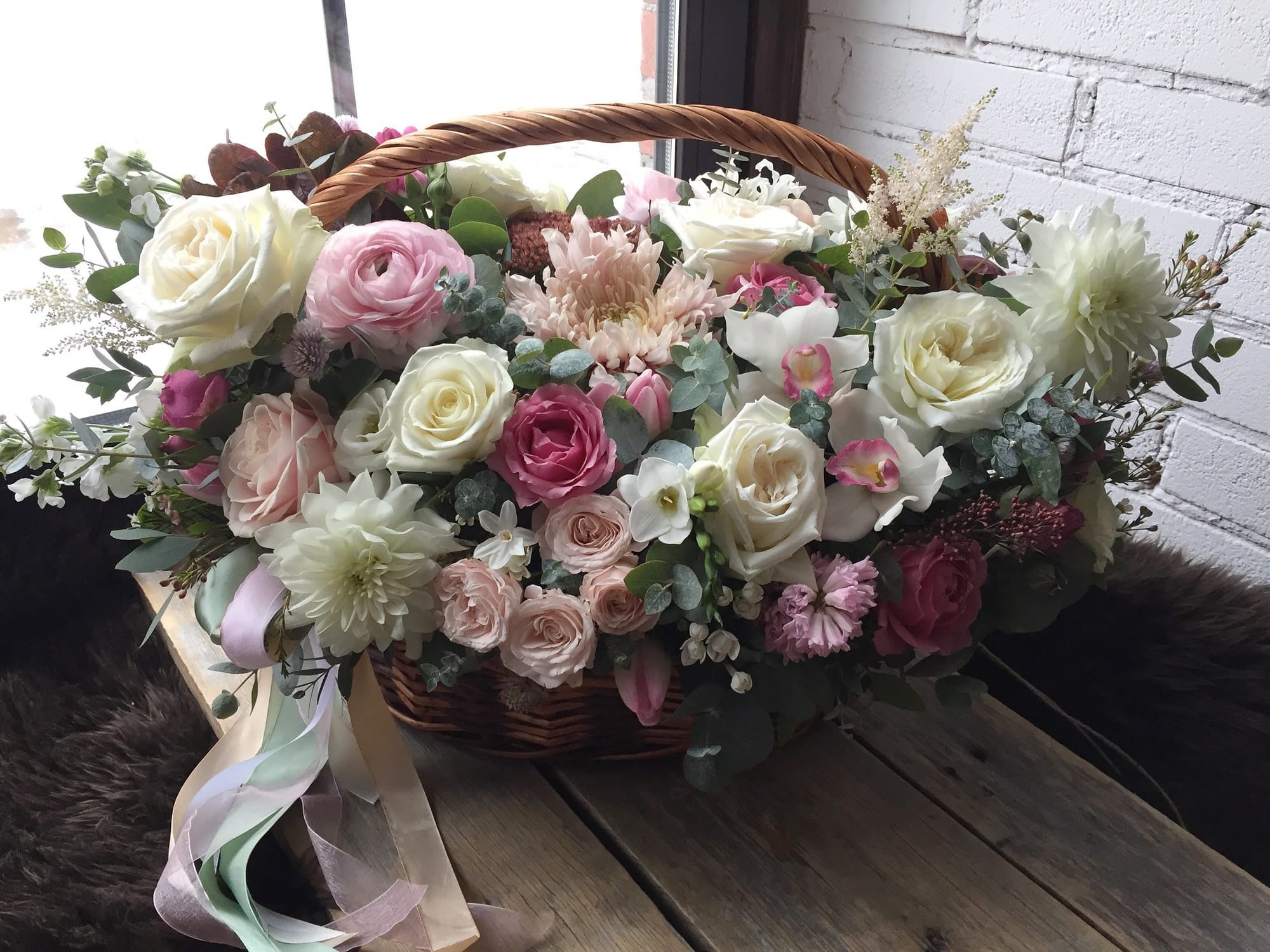 Basket arrangement of pink and white roses with mixed blooms and ribbon
