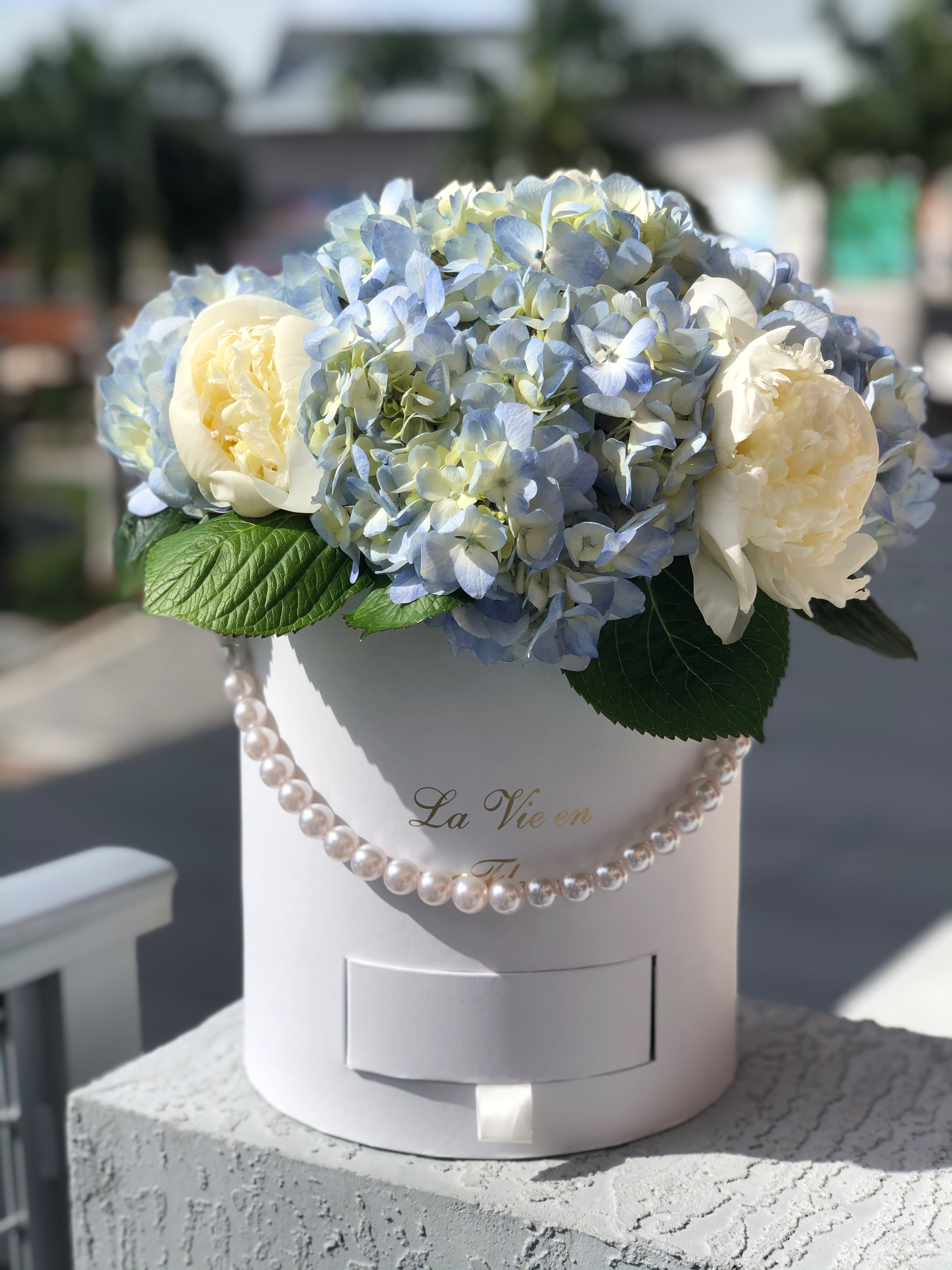 Blue hydrangeas and white peonies in a white hat box with pearl trim
