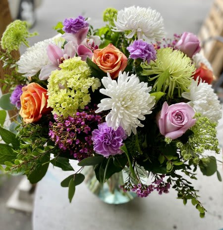 Mixed arrangement of roses, chrysanthemums, and carnations in a clear glass vase