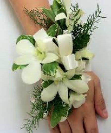 White floral wrist corsage with green foliage on a person's wrist