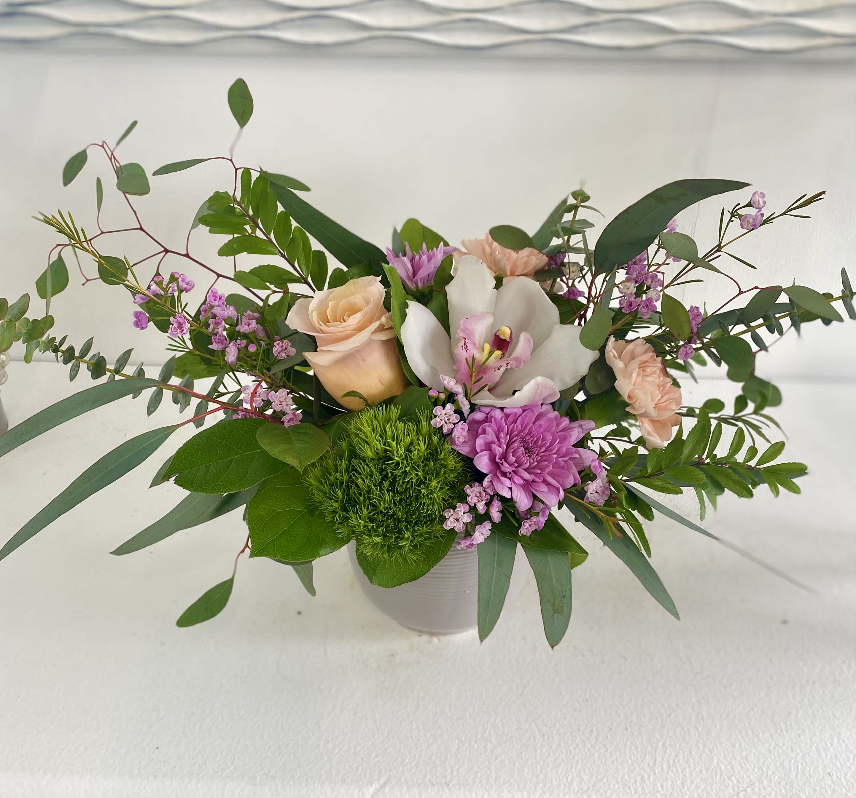 Mixed floral arrangement in a white vase with roses, orchids, and purple blooms