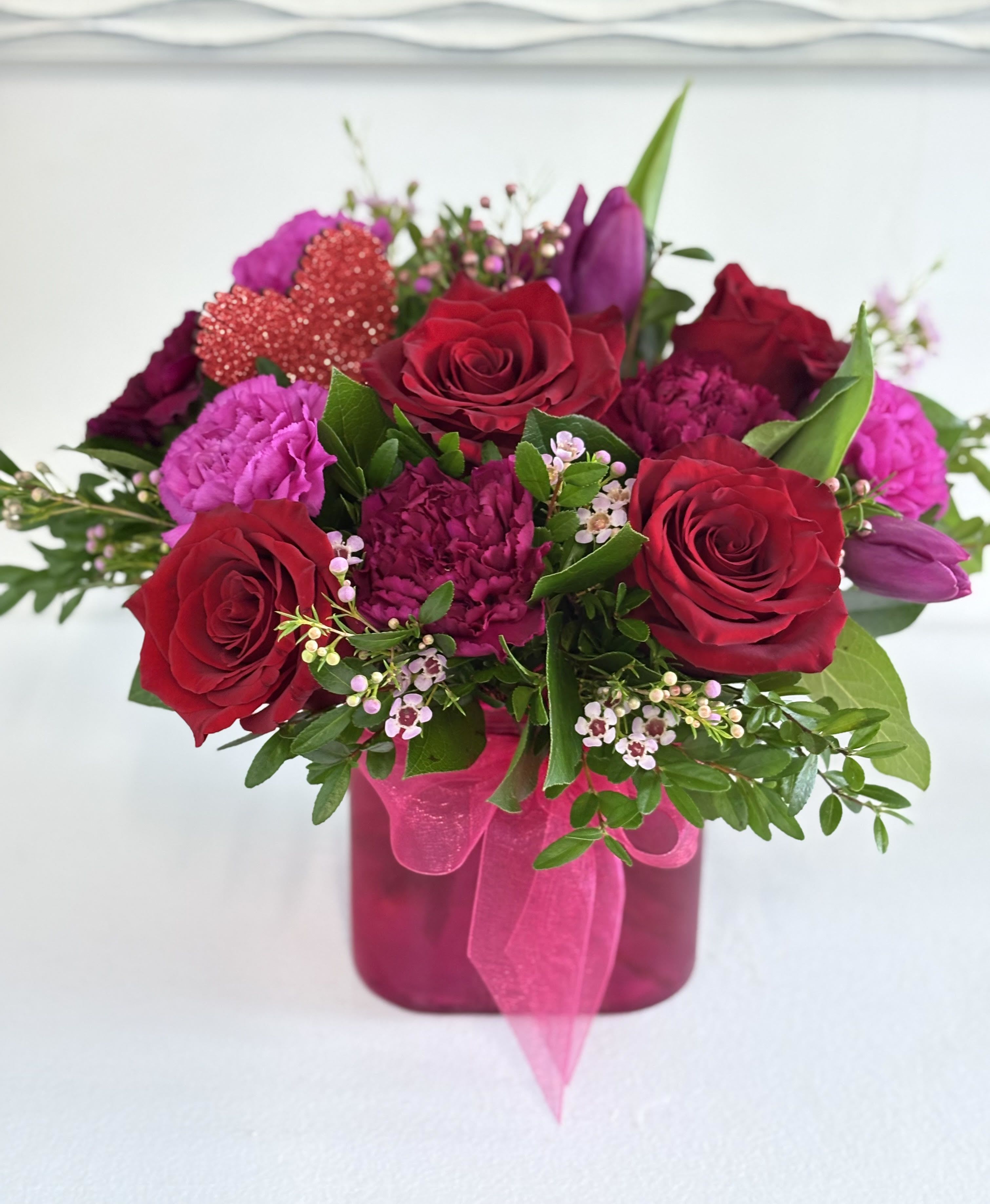 Bouquet of red roses and pink flowers in a magenta vase with ribbon