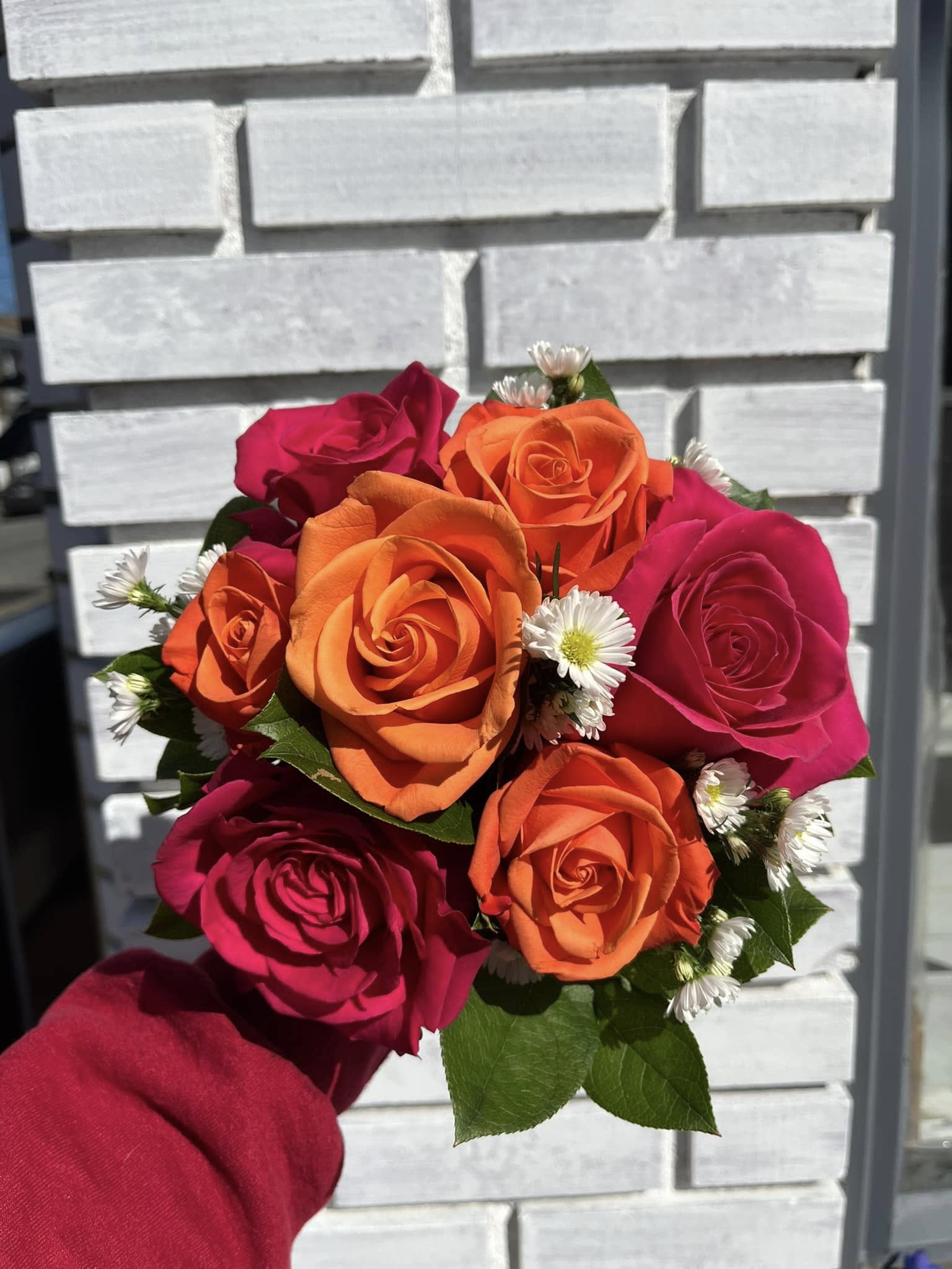 Handheld bouquet of orange and pink roses with small white daisies