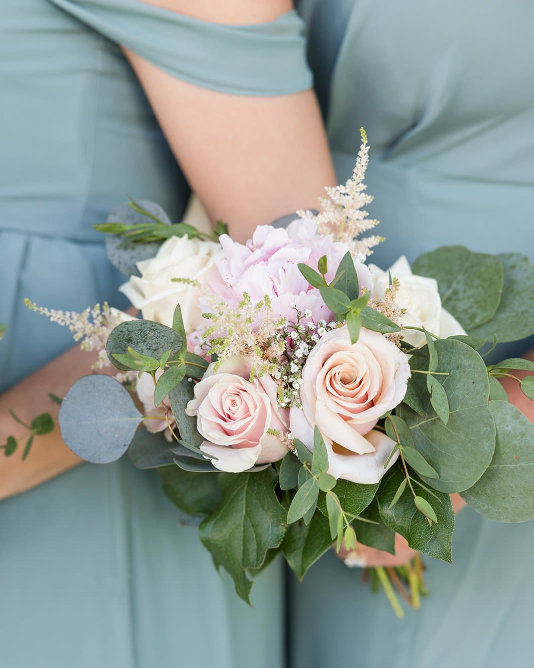Handheld bouquet of pale pink and white roses with greenery