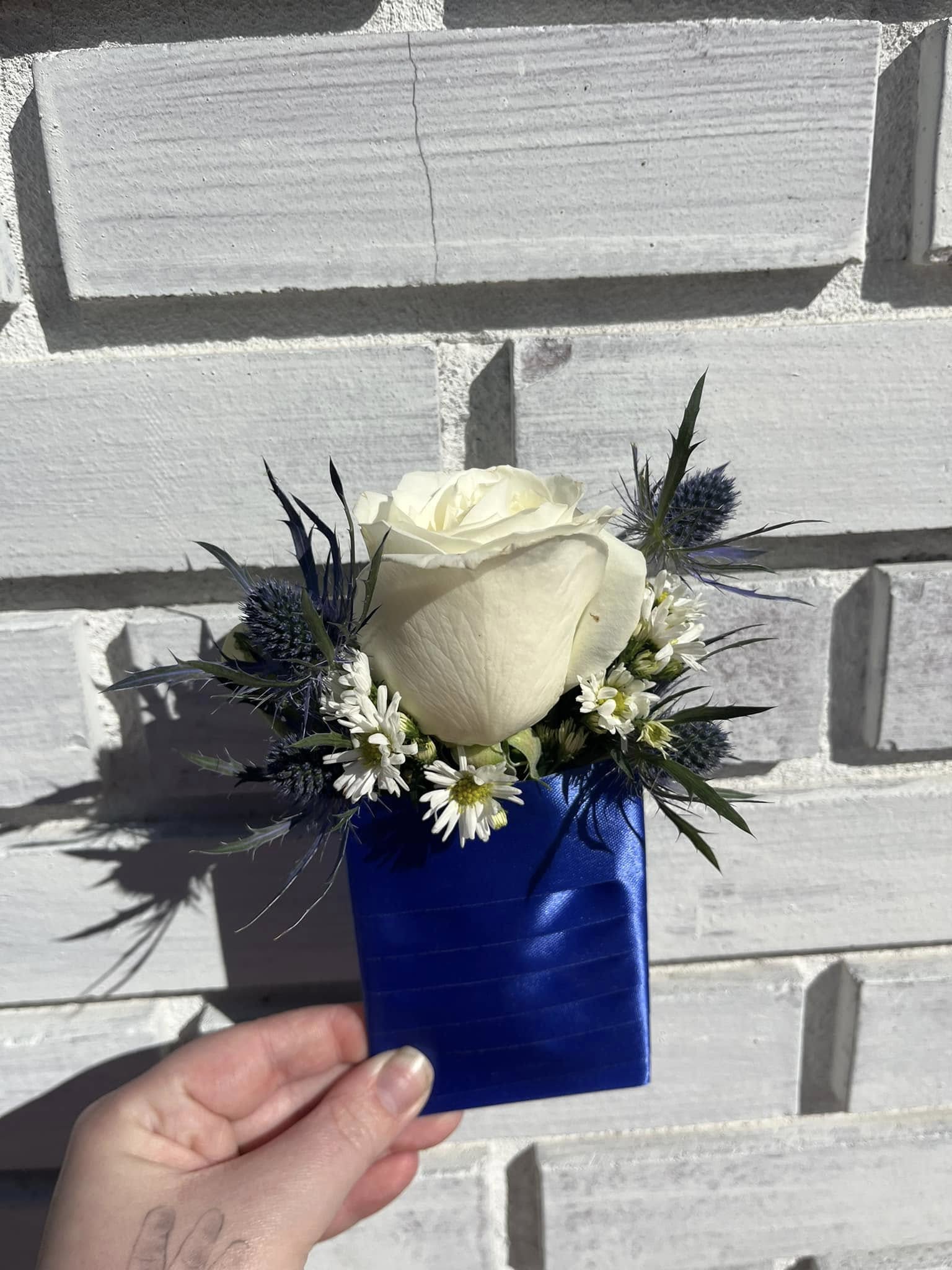 White rose boutonniere with blue ribbon wrap and small white daisies