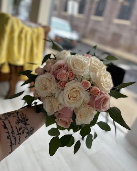 Handheld bouquet of white and blush roses with greenery
