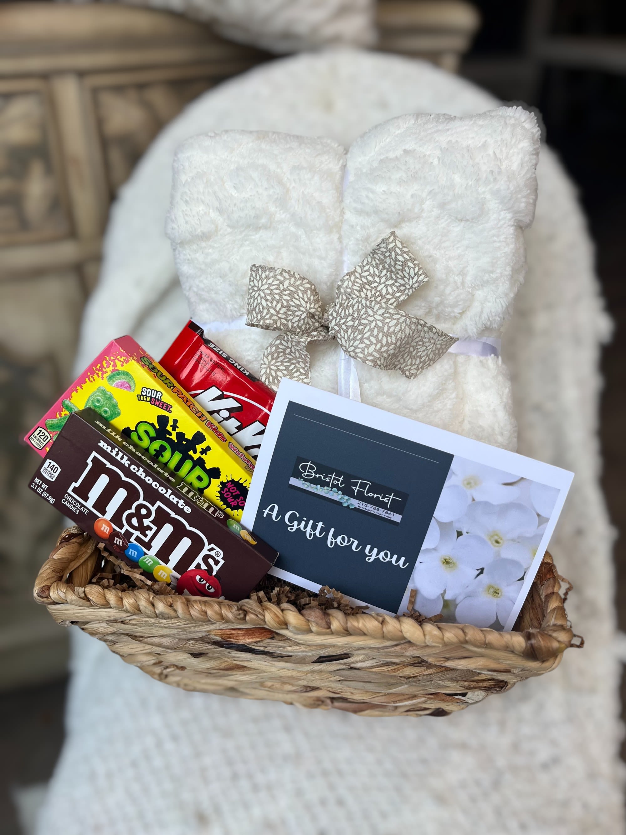 Gift basket with a white plush blanket, candy boxes, and a florist card