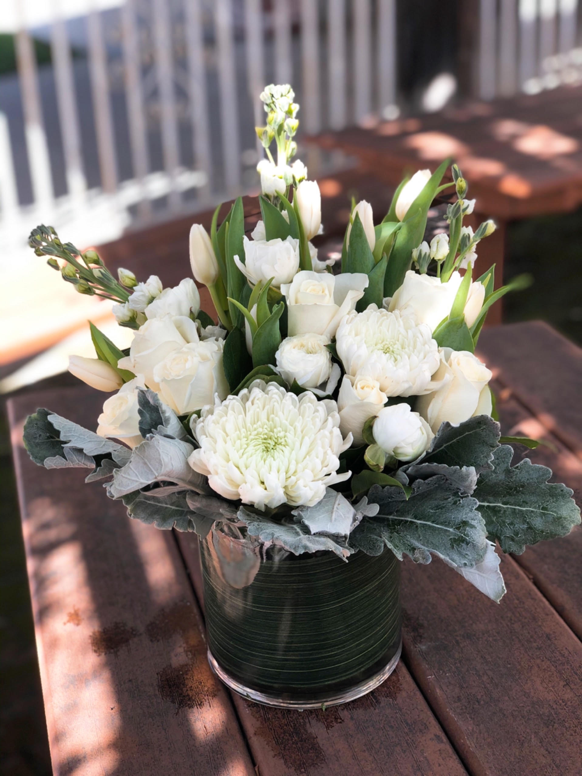Purity - - 3 White Stock (or White Snapdragons) - 6 White Roses - 2 White Spider Mums - 5 White Tulips - Greenery  - Dusty Millers - 6 x 6 Inches Clear Cylinder Vase