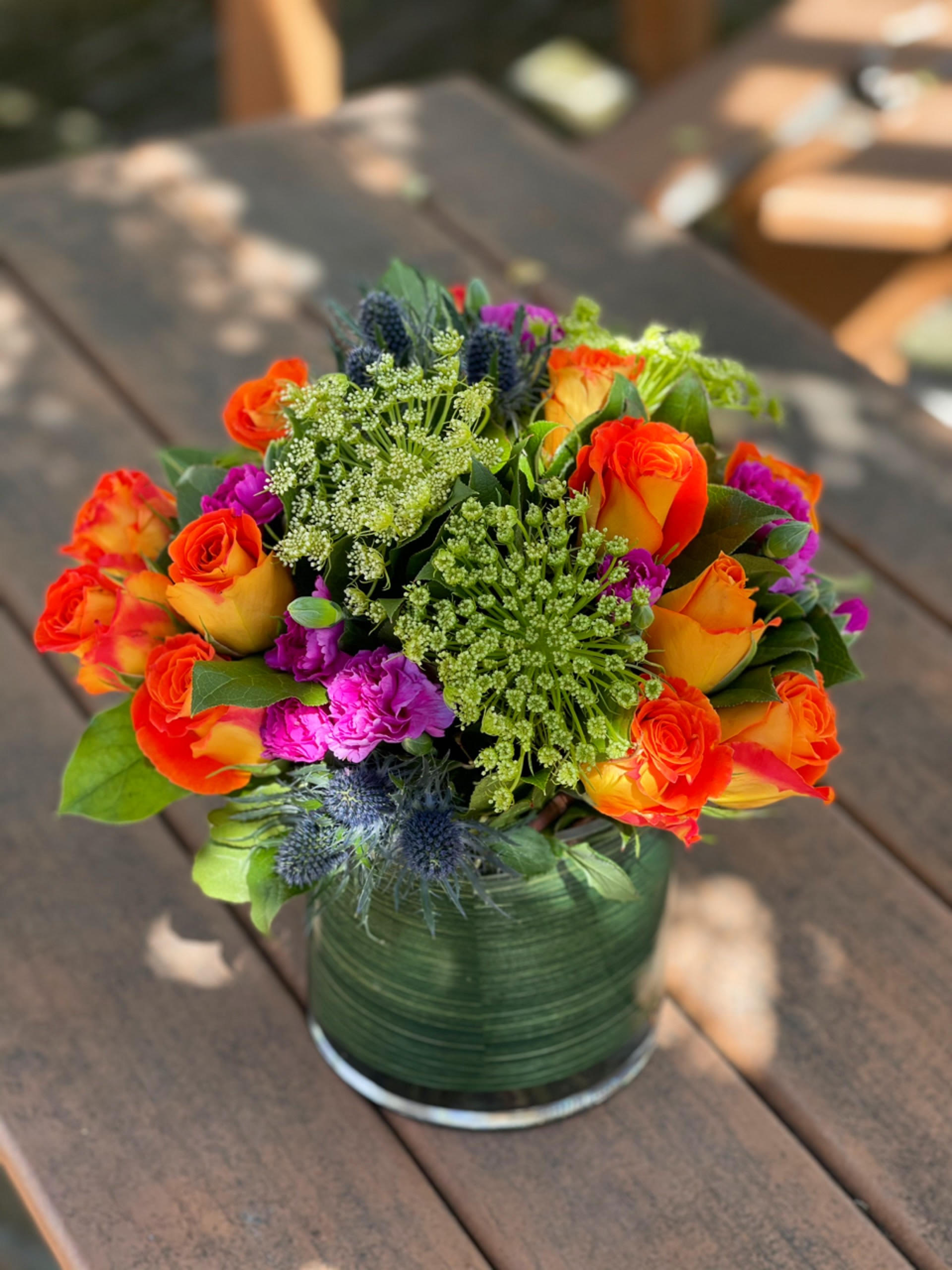 Bright mixed bouquet of orange roses and purple flowers in a glass vase