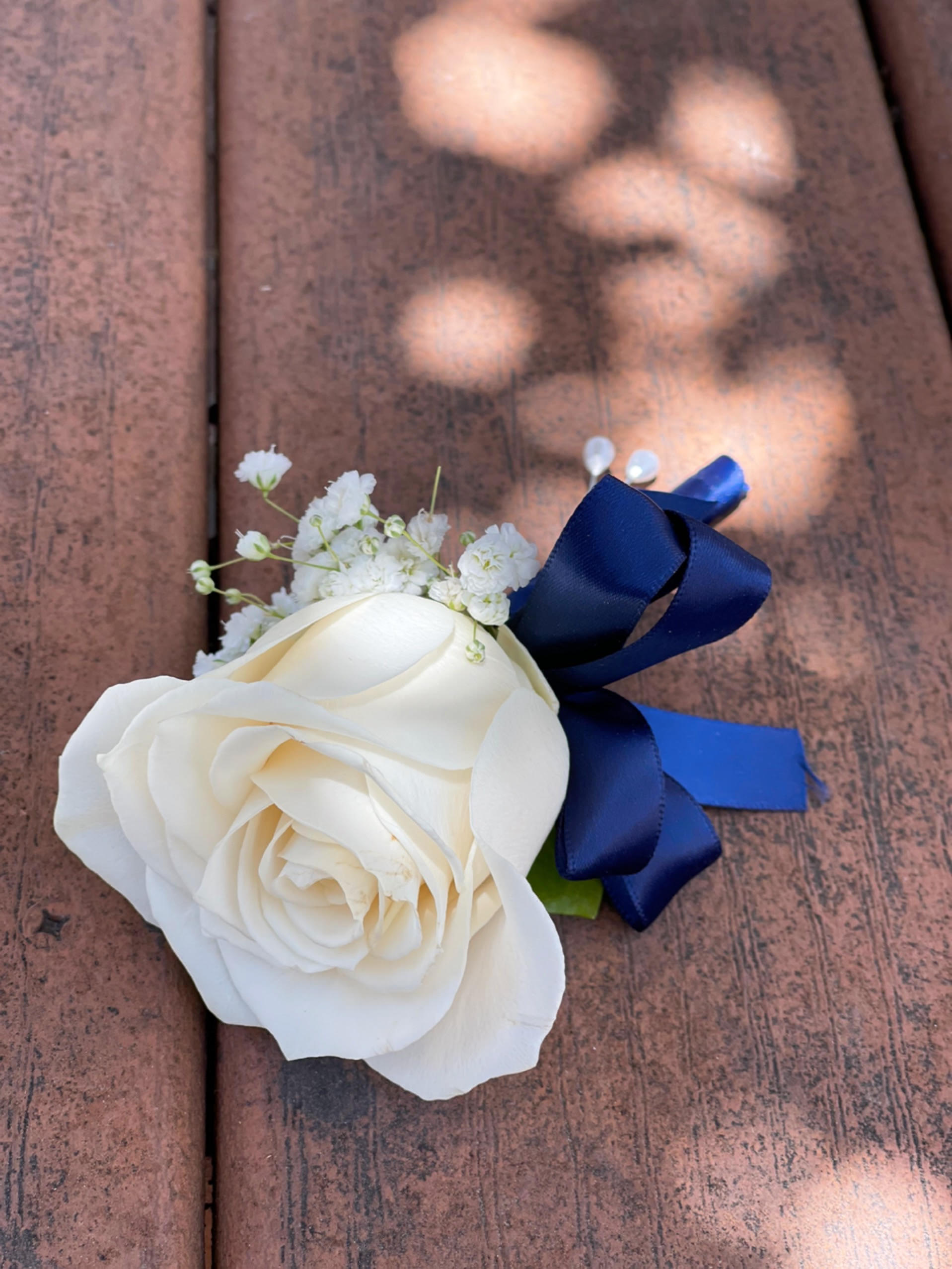 White rose boutonniere with baby's breath and a blue ribbon