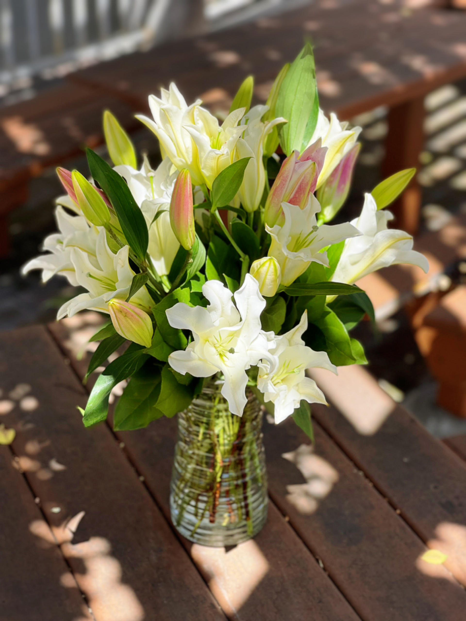 White lilies in a clear glass vase on a wooden table