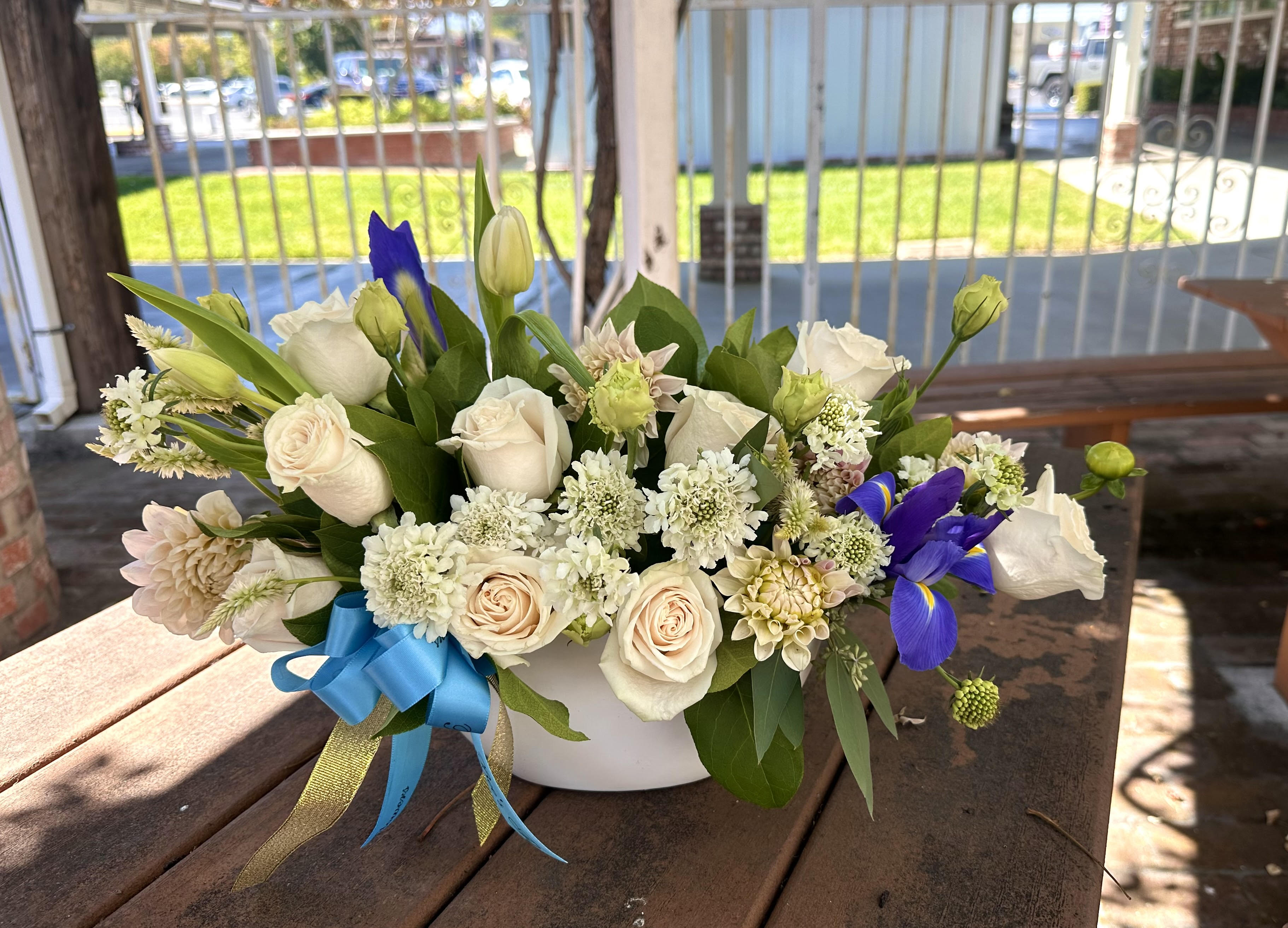 White and cream flower arrangement with blue irises in a white bowl vase
