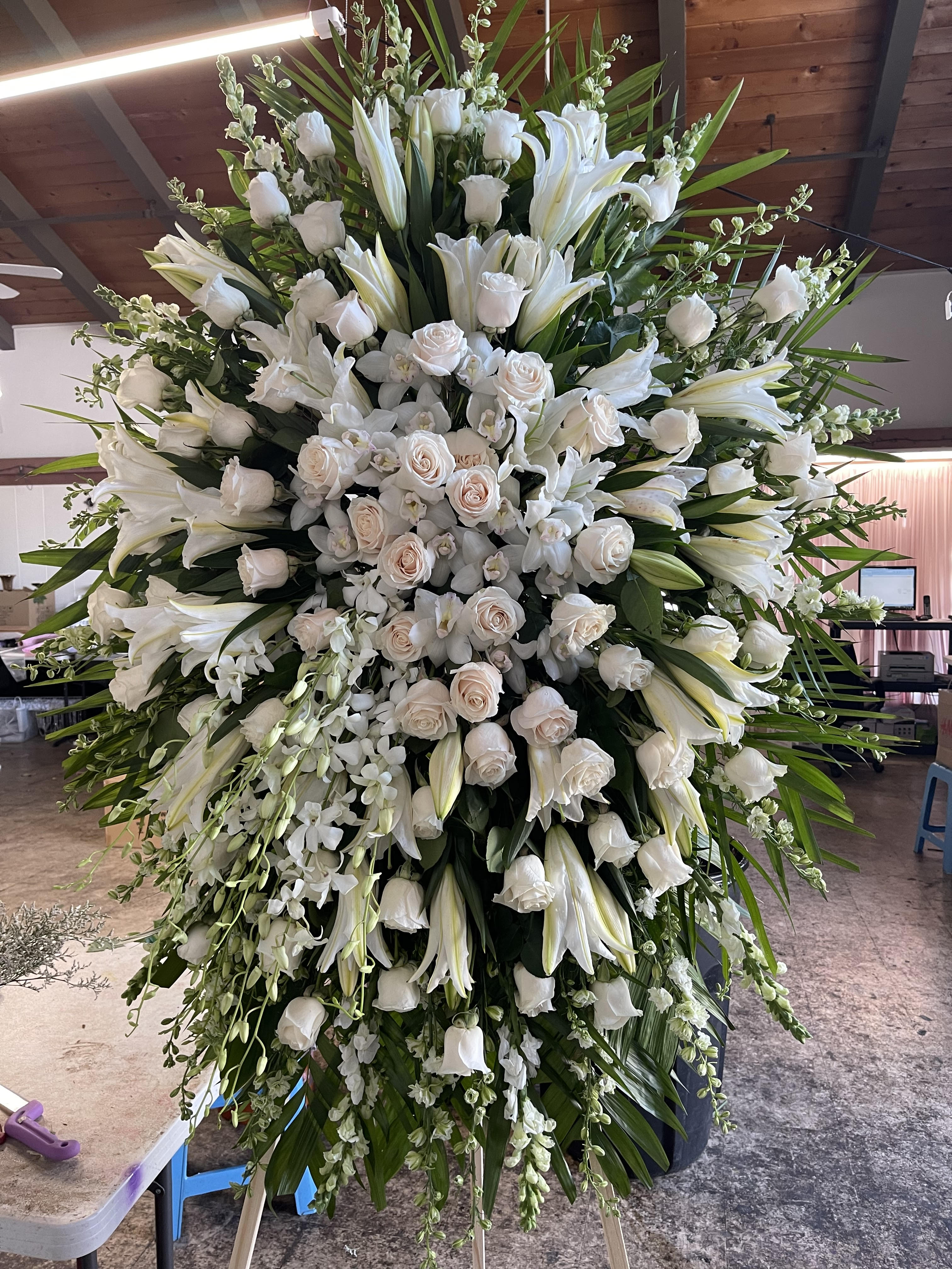 Large white funeral spray with roses and lilies on an easel