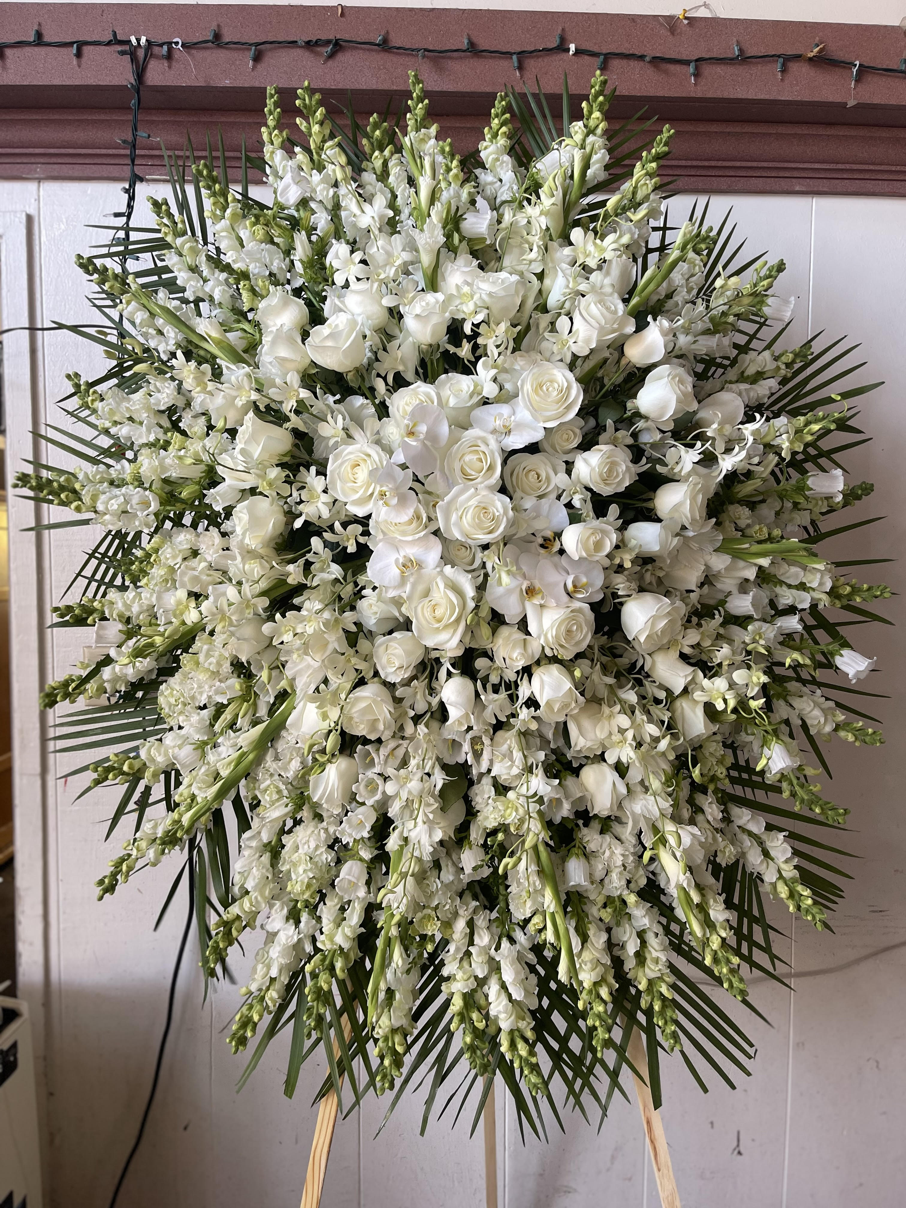 Large white funeral spray with roses and orchids on a standing easel