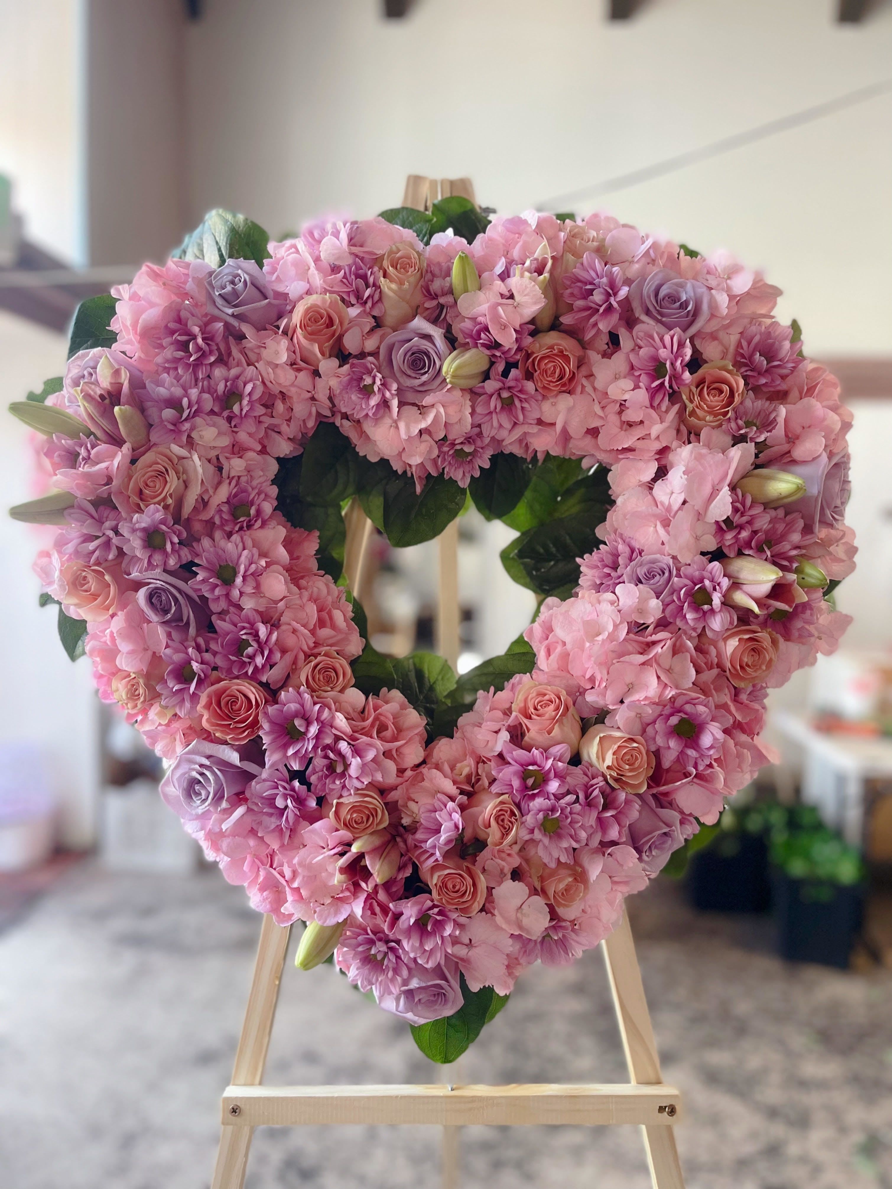Heart-shaped pink floral wreath on a wooden easel