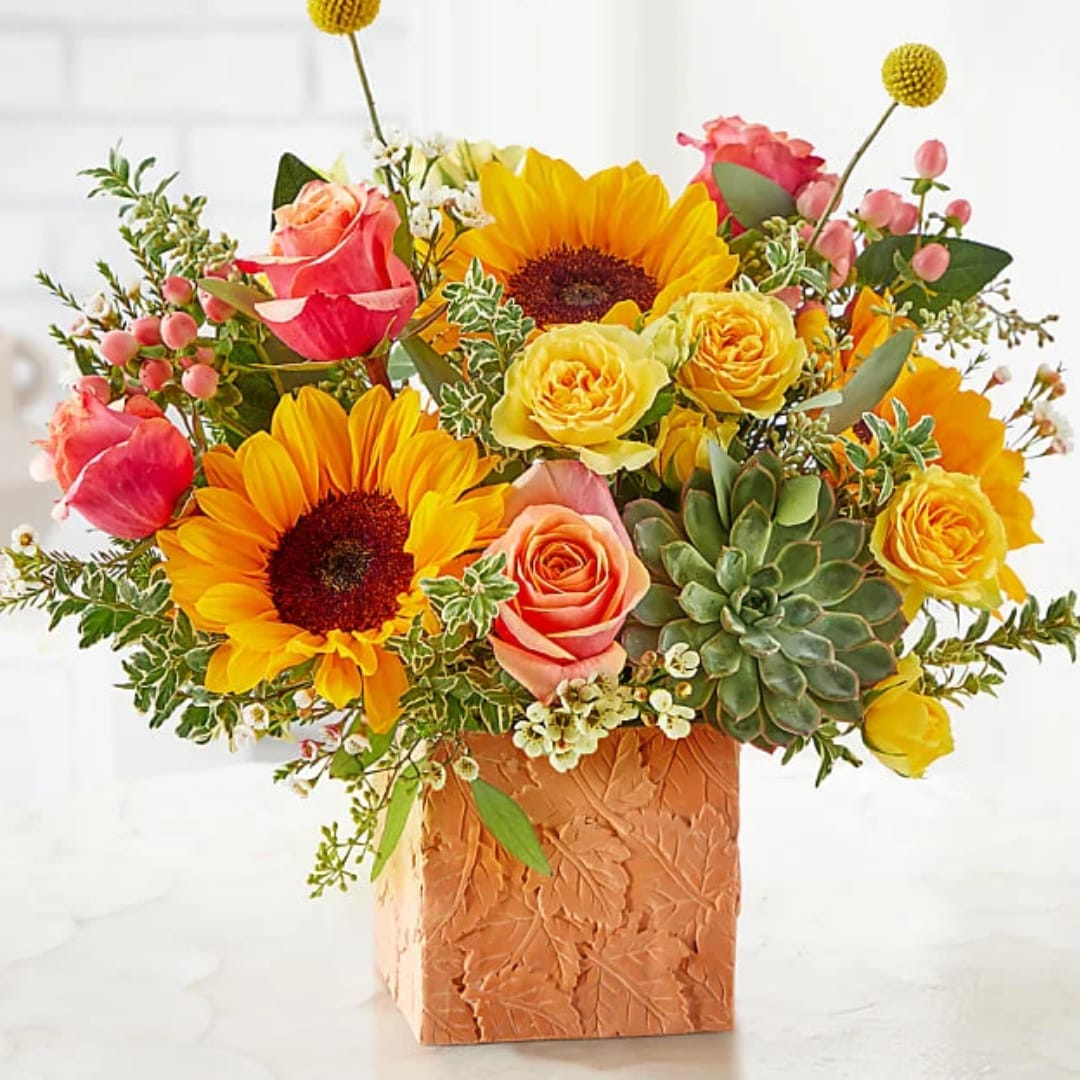Bright bouquet of sunflowers, roses, and succulents in a textured square vase