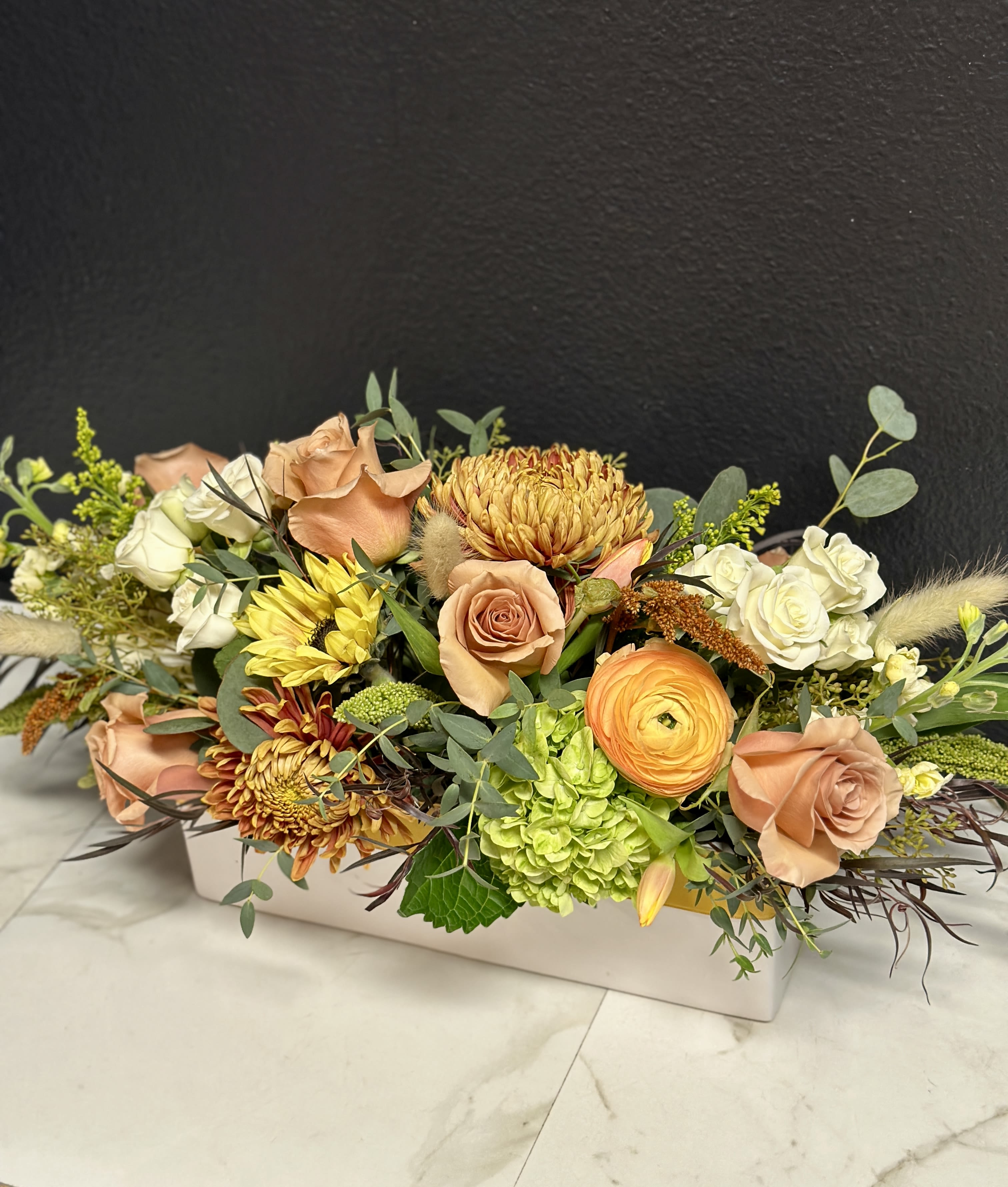 Low floral arrangement with peach roses, white blooms, and yellow chrysanthemums in a white box.