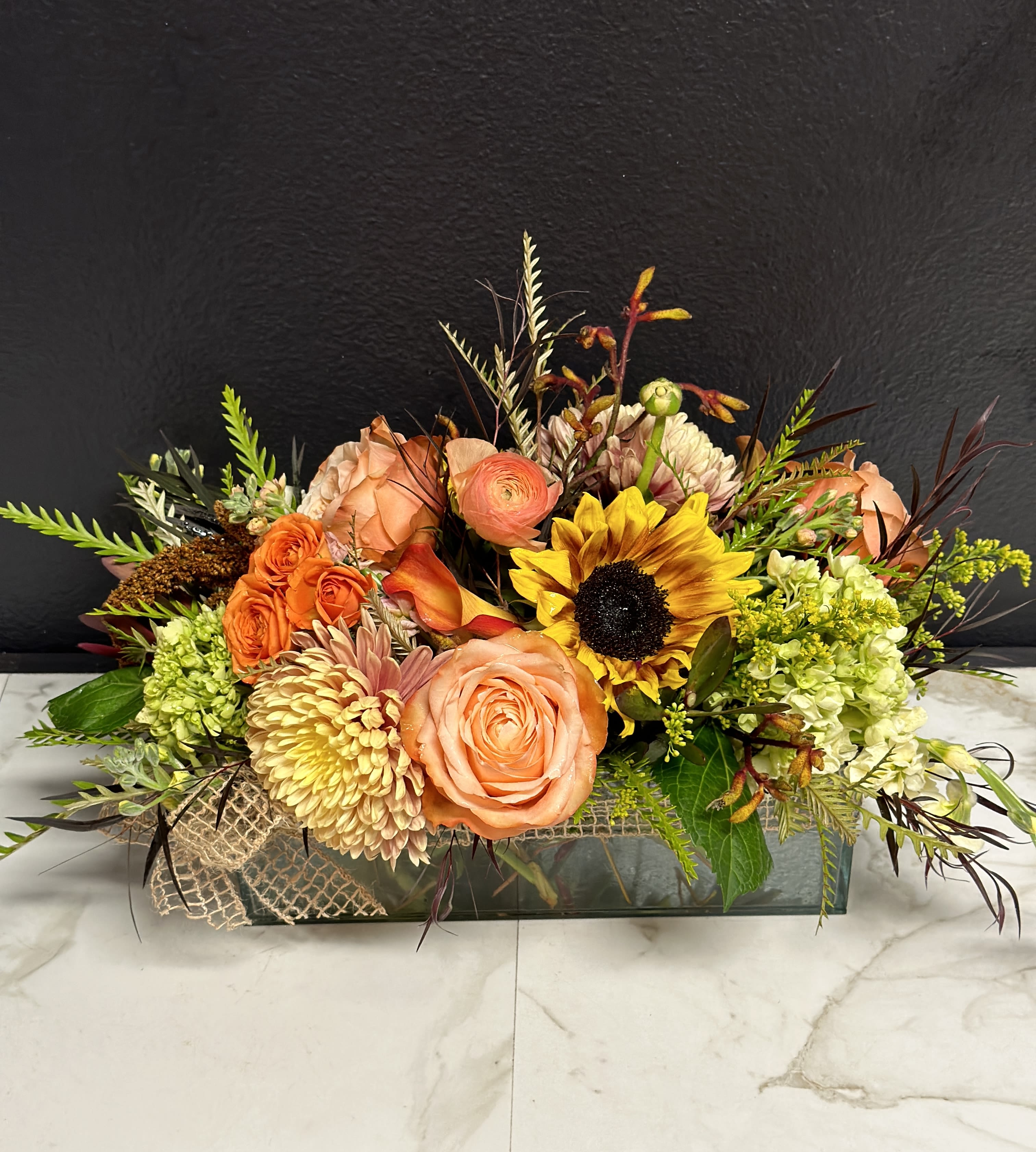 Mixed floral arrangement with peach roses and a sunflower in a low rectangular vase
