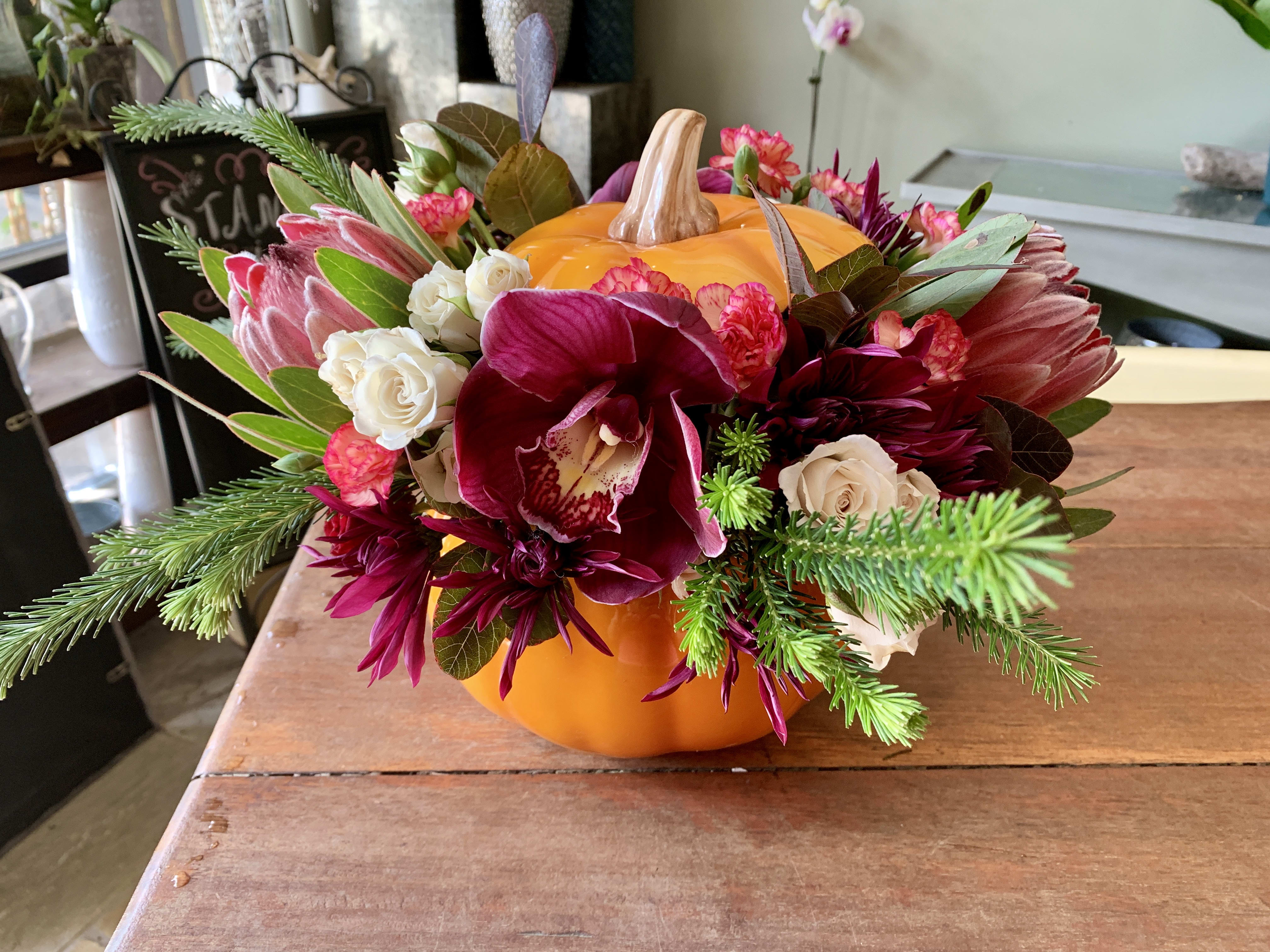 Floral arrangement in a pumpkin-shaped container with burgundy and white blooms