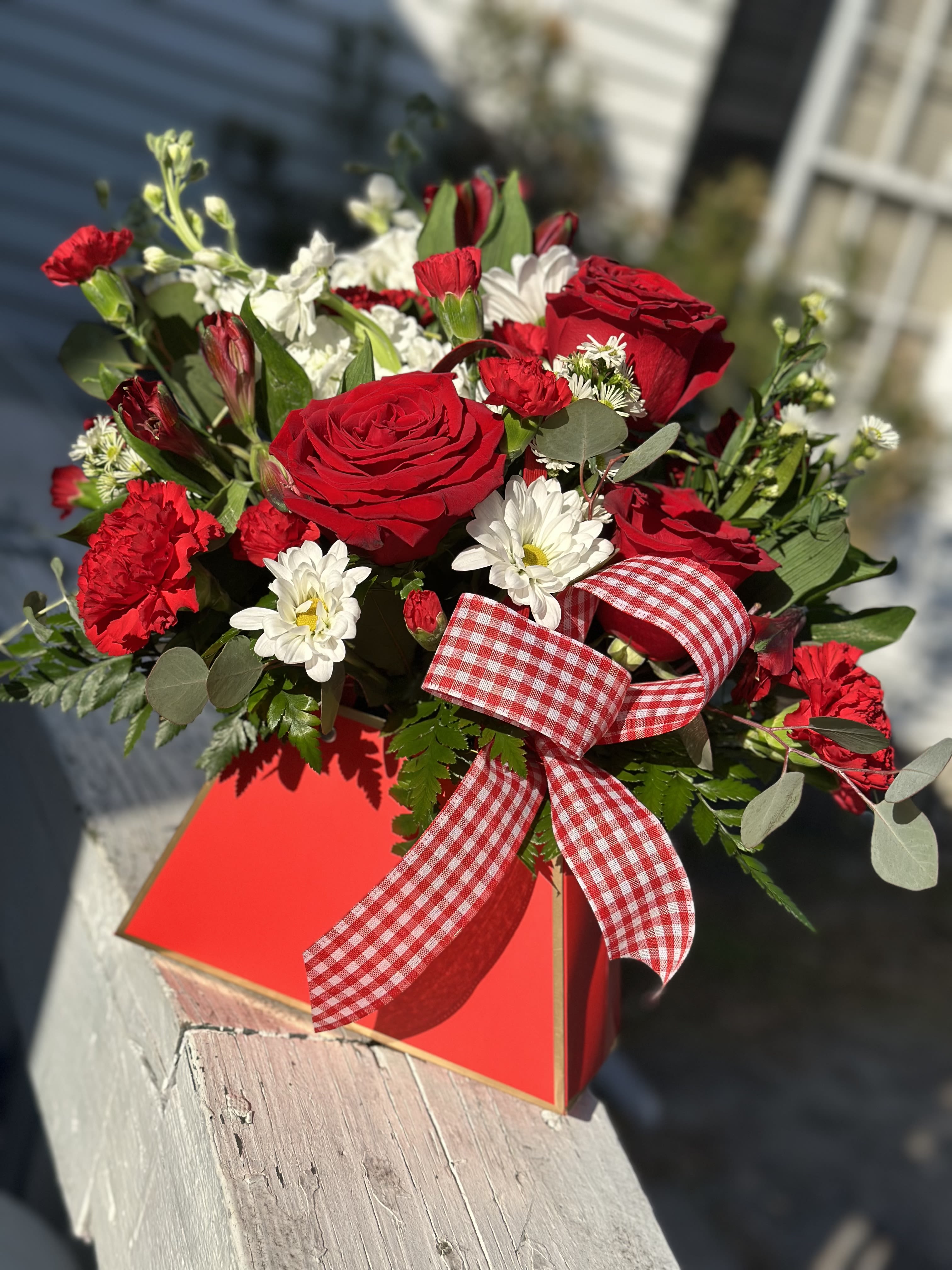 Red roses and white daisies in a red gift box with a gingham ribbon