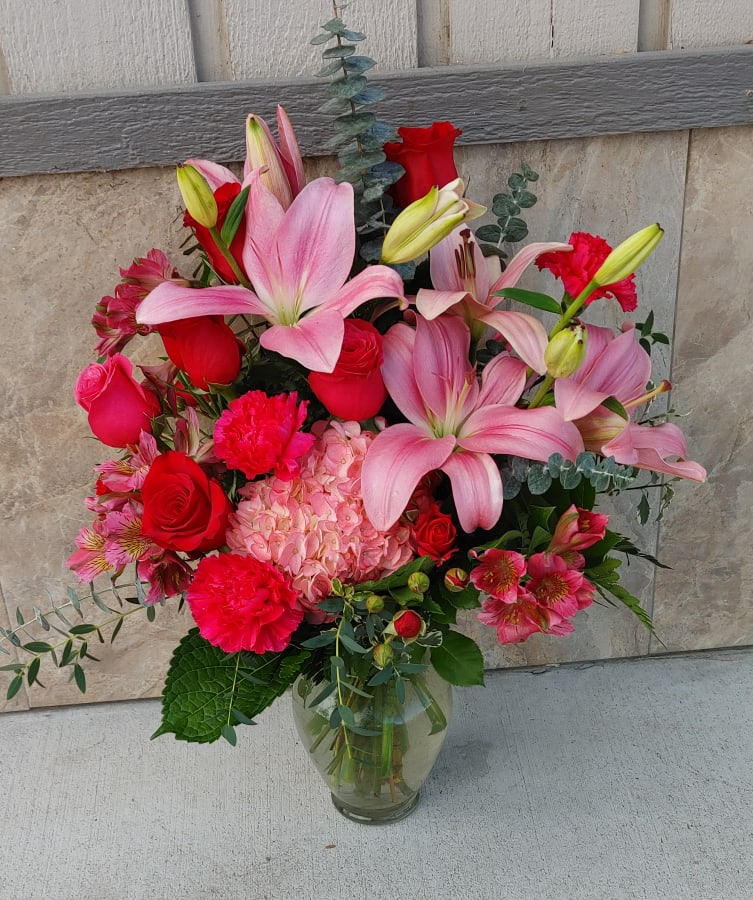 Bouquet of pink lilies, red roses, and pink hydrangea in a glass vase