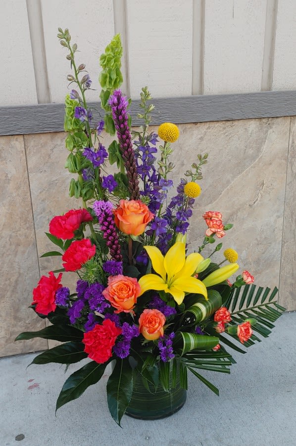 Tall mixed flower arrangement in a dark vase with yellow lilies and orange roses