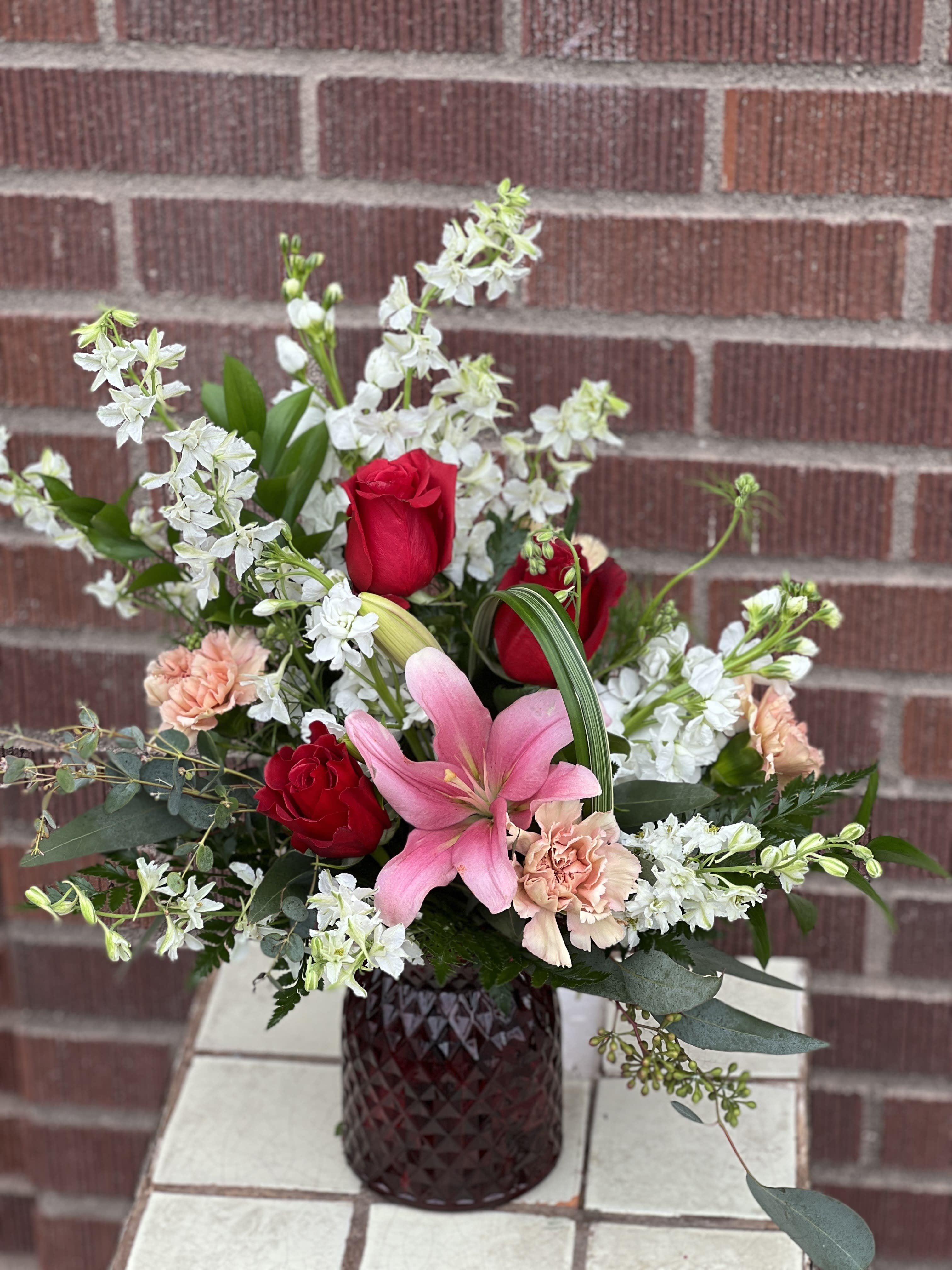Pink lily and red roses in a dark glass vase