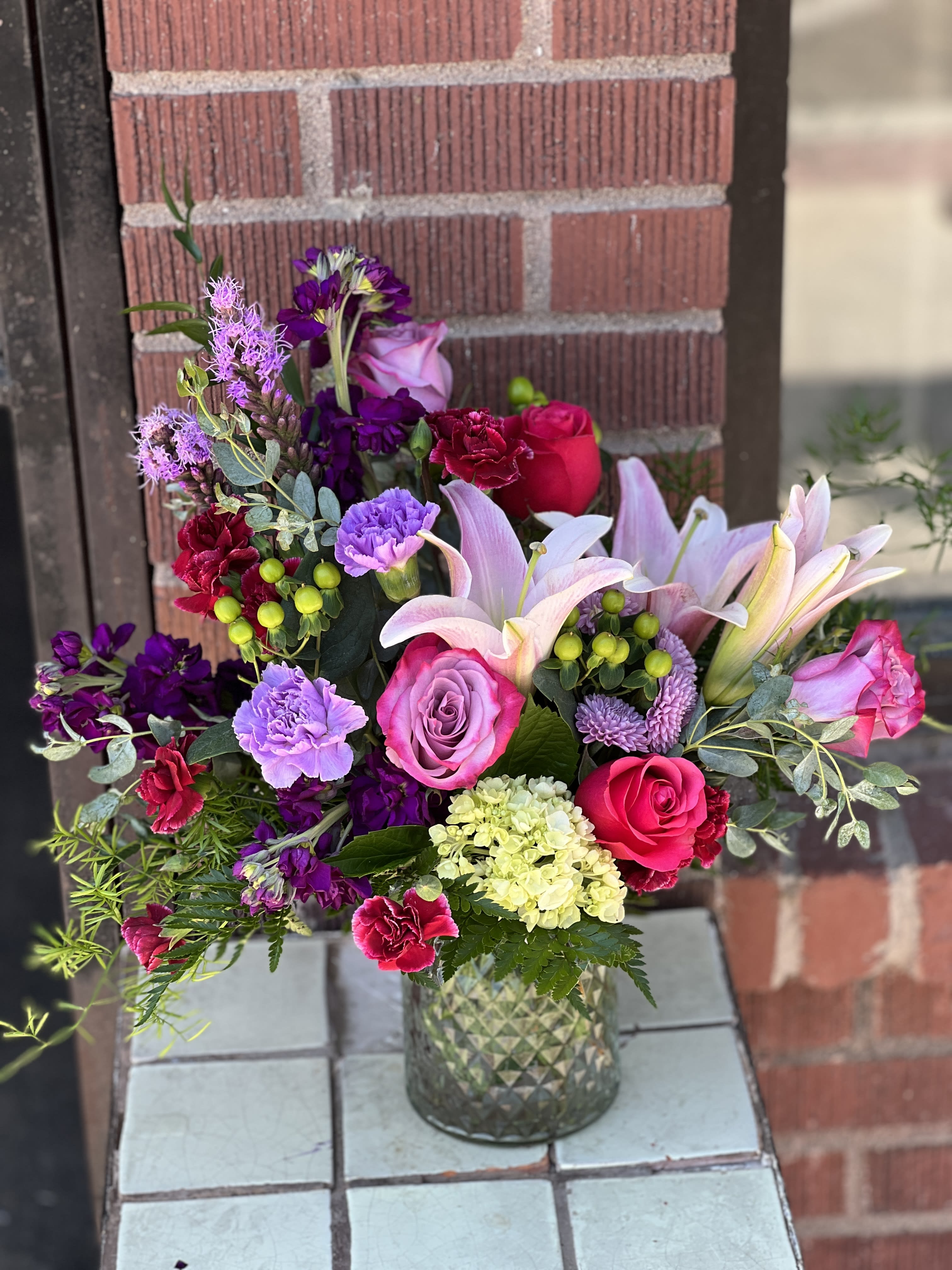 Mixed bouquet of pink, purple, and white flowers in a glass vase