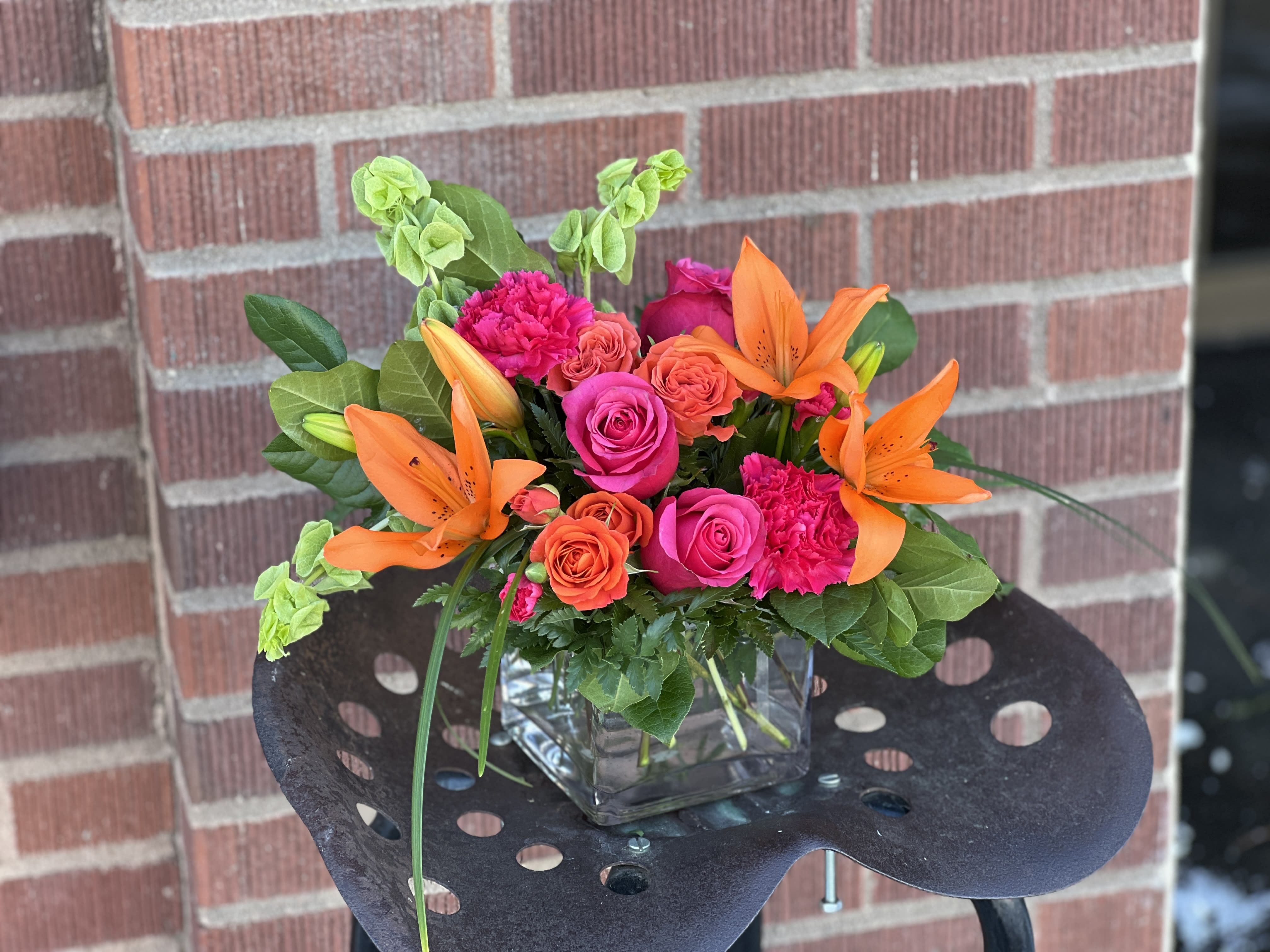 Bright bouquet of orange lilies and pink roses in a glass cube vase