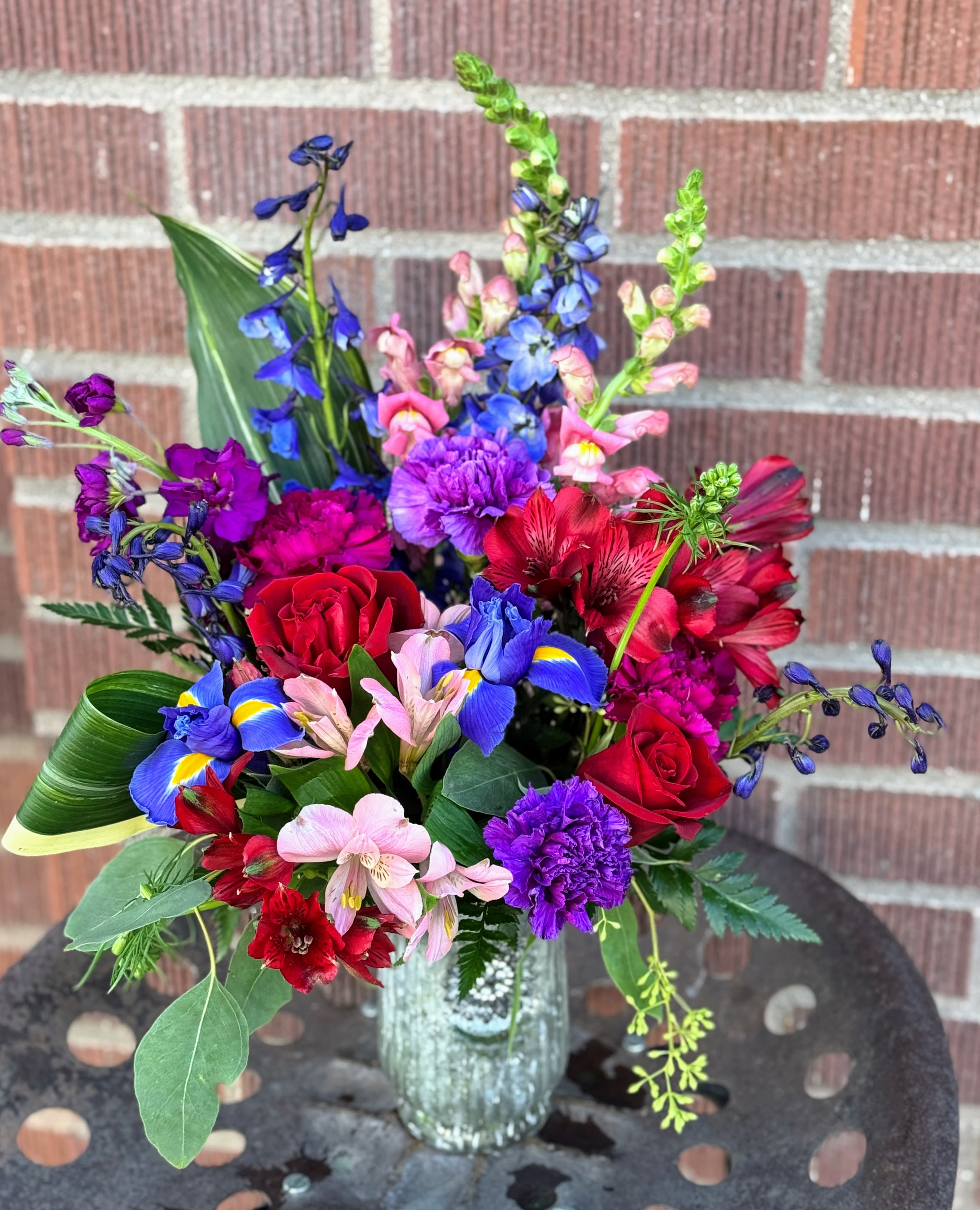 Colorful mixed bouquet with roses, irises, and alstroemeria in a glass vase