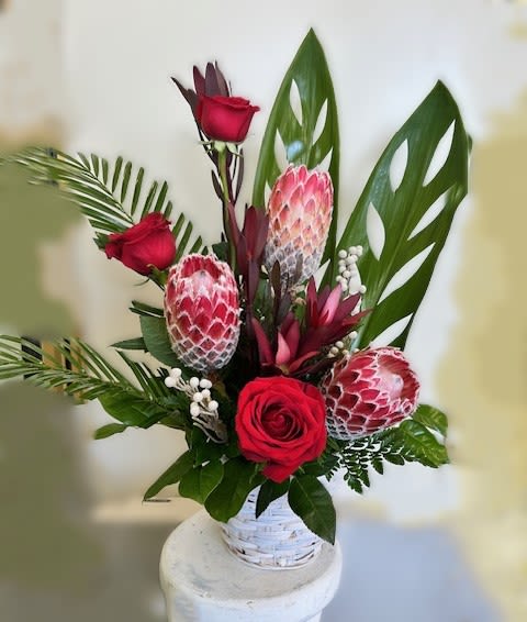 Red roses and pink protea in a white basket vase