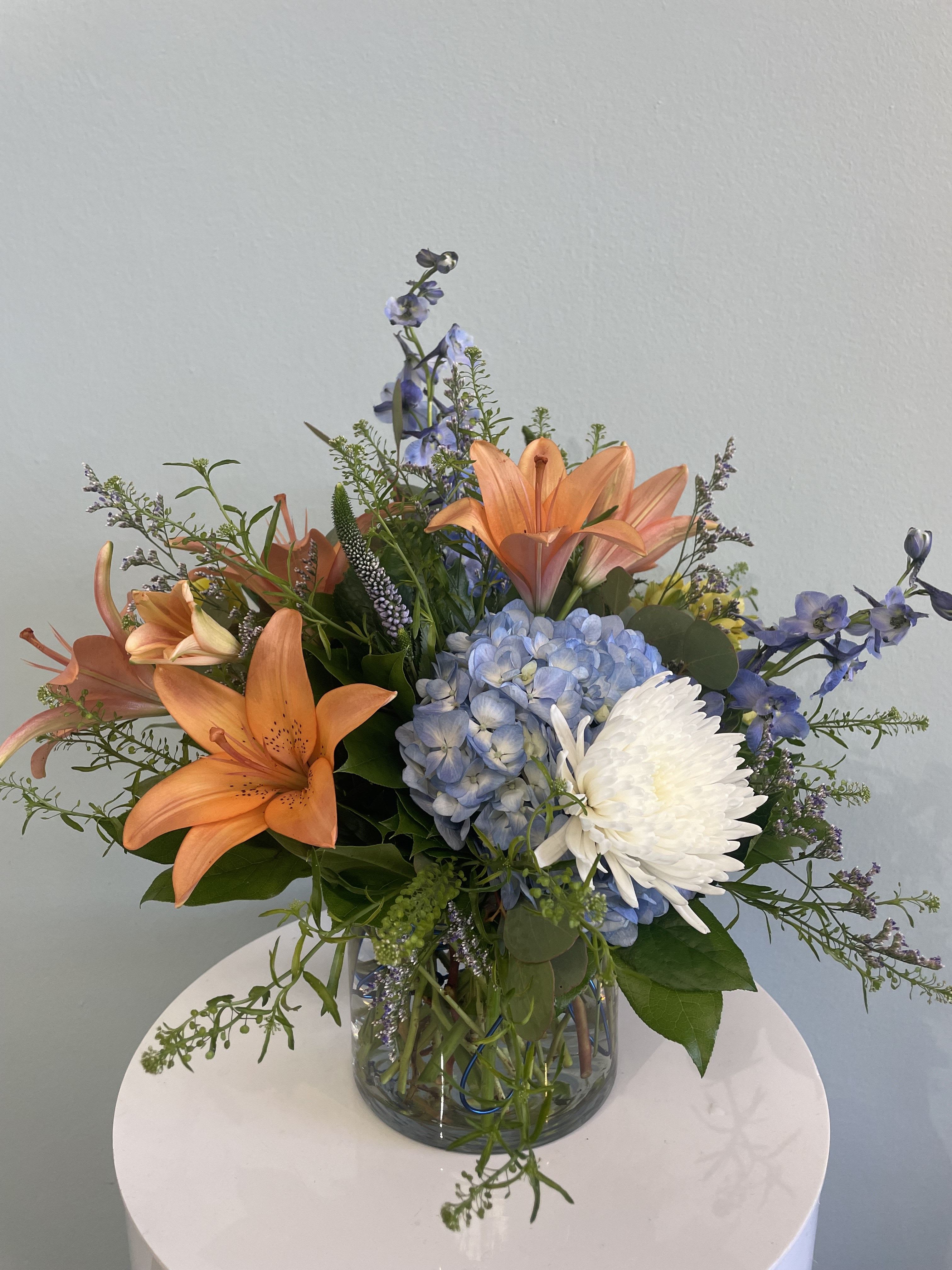 Water Lilies - This beautiful low-profile arrangement is perfect for any occasion. This stunning mix of lilies, fuji mums, delphinium, and a large blue colored hydrangea brings a tranquil vibe into any space. 
